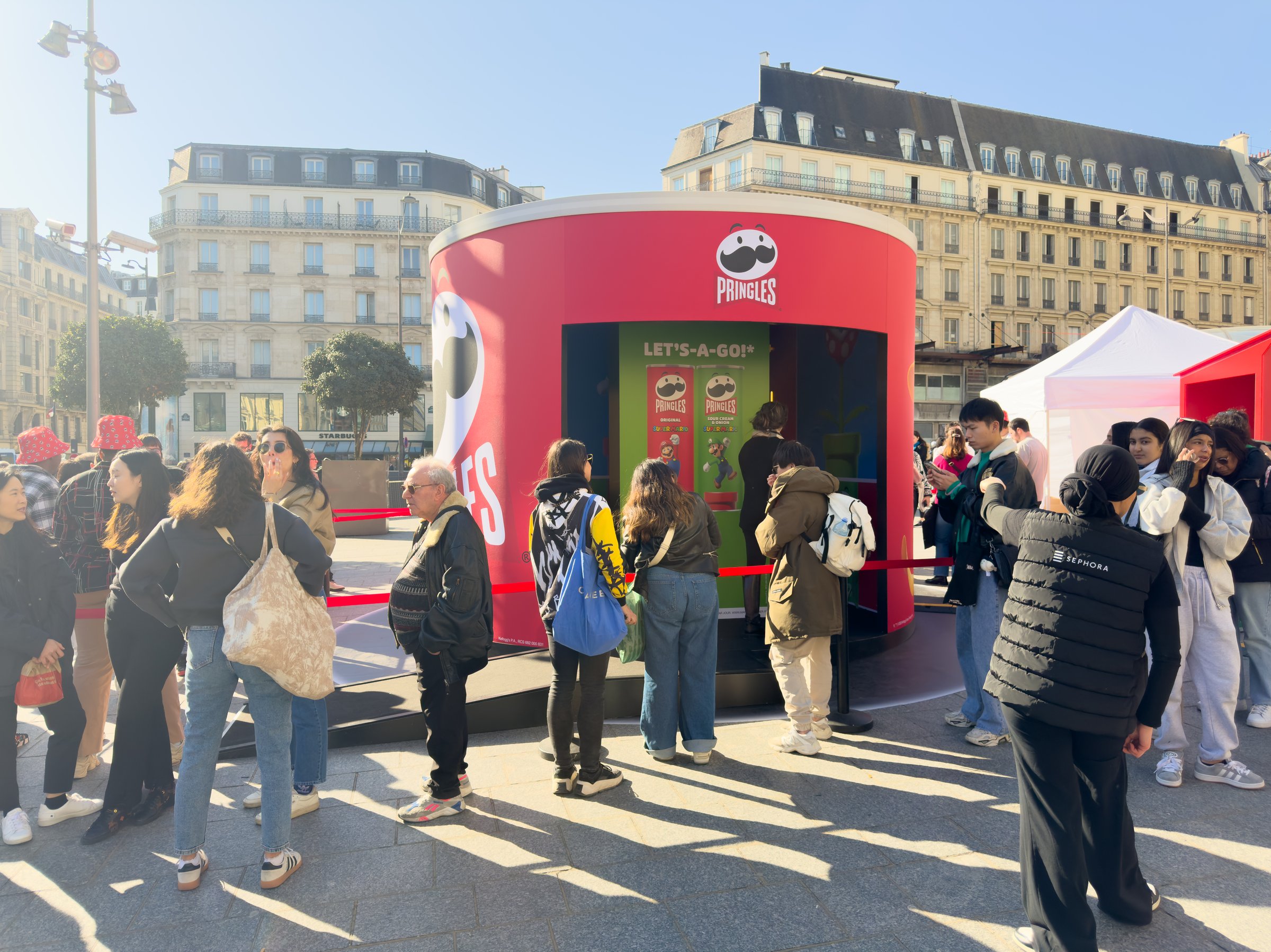 Paris,France-06-03-2025 Excited visitors line up outside a colorful pop-up stand, enjoying tasty treats and the festive atmosphere on a sunny day in a bustling city square.