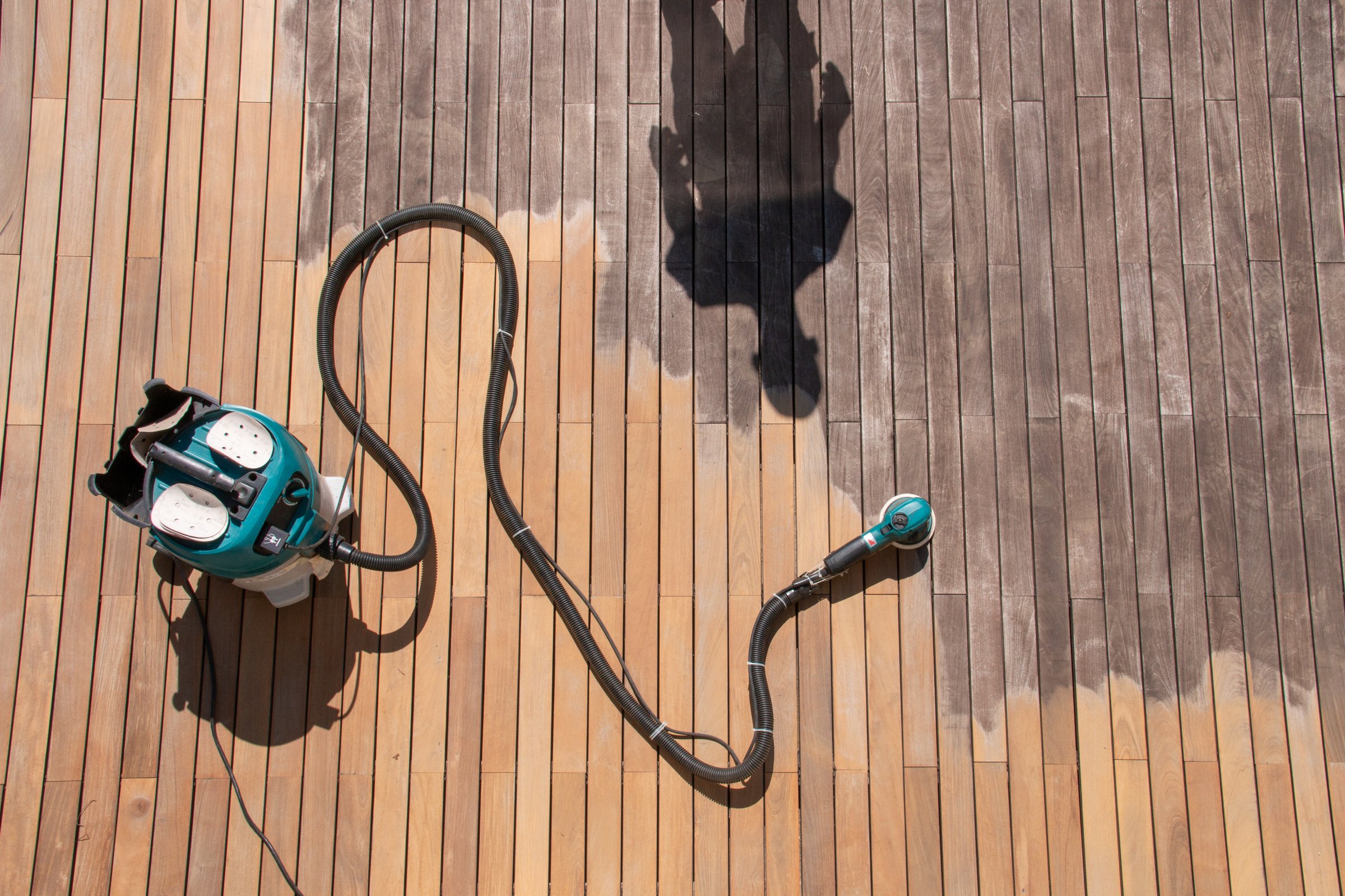 Hardwood deck renovation tools concept, electric sander and dust collector on the exterior terrace with the silhouette of restore worker, before after effect during work process