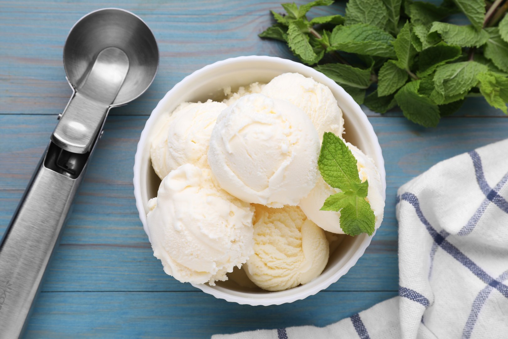 Delicious vanilla ice cream with mint and scoop on light blue wooden table, flat lay