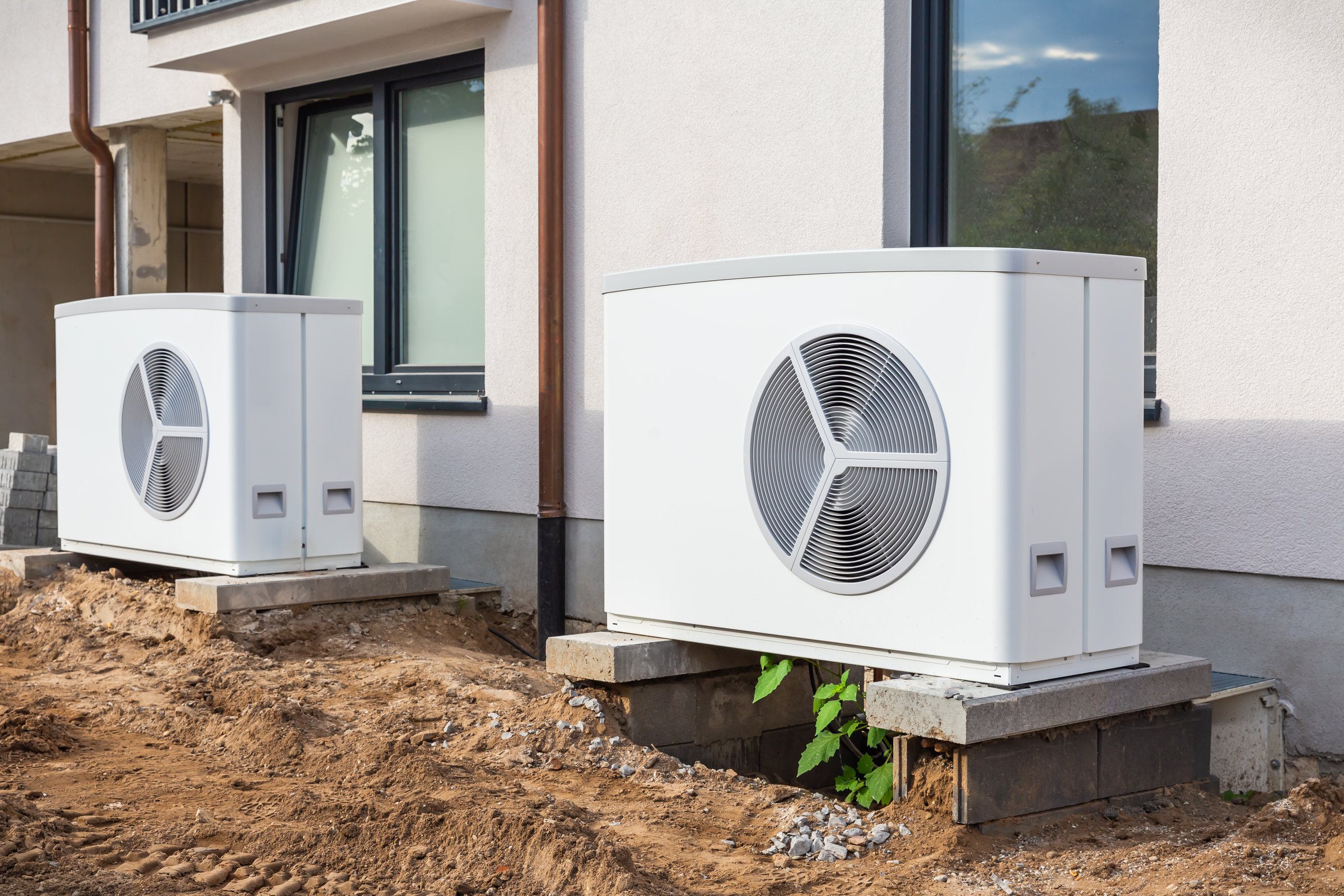 Two air source heat pumps installed outside of new and modern city house under construction, green renewable energy concept of heat pump