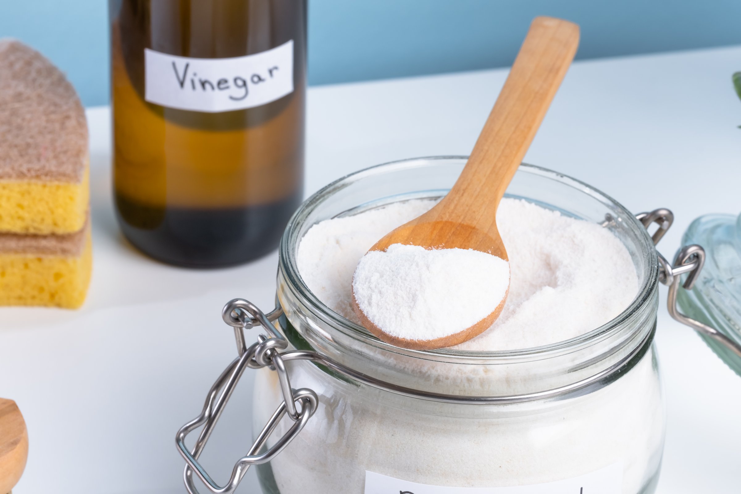 Baking soda in a glass jar with a wooden spoon on a clean countertop for kitchen use and baking. A wooden spoon rests on the jar.