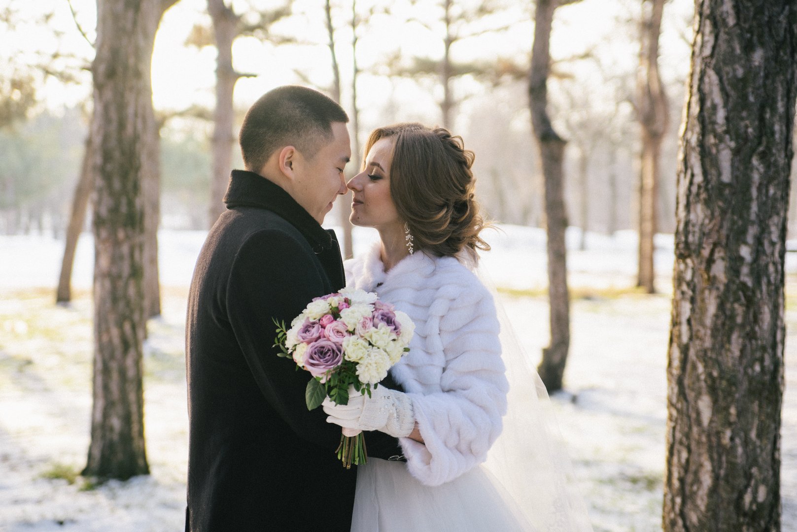 The bride and groom are kissing in the winter forest