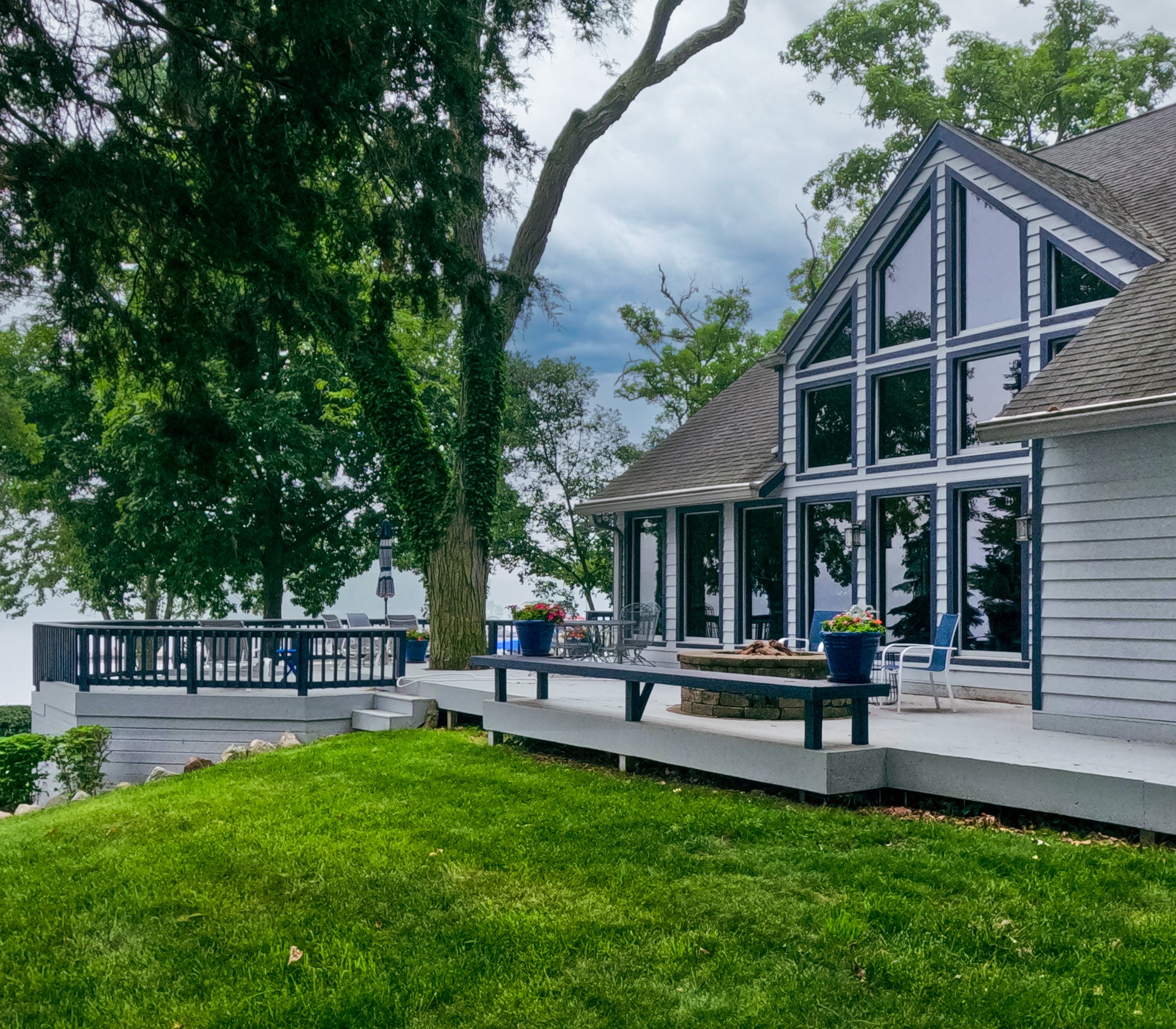 Upscale modern residential home on the lake. Vaulted rooftop with large windows and a deck with fire pit and hot tub. Large old growth trees and grassy green yard.