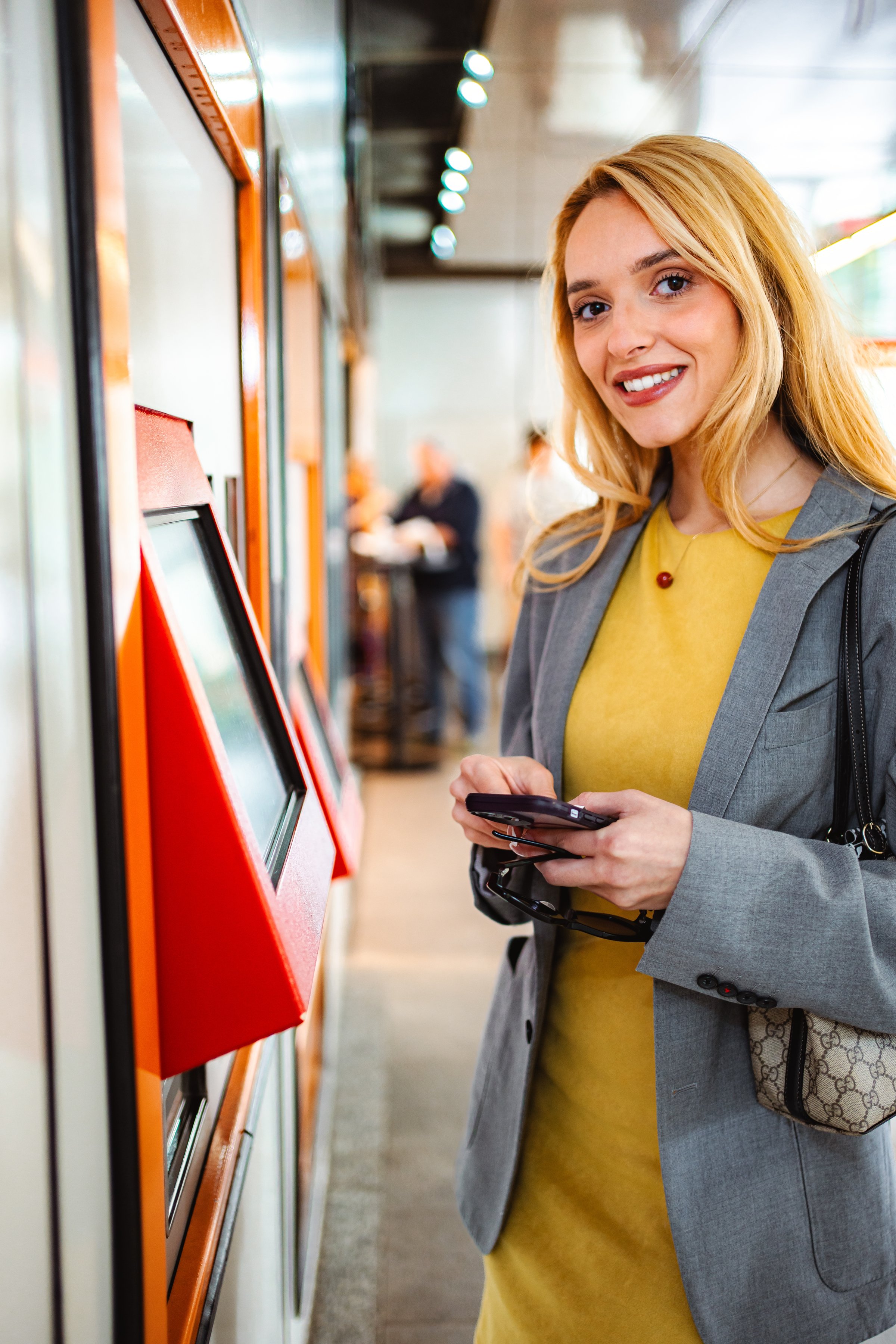 Young woman smiling, standing by a vending machine, checking her smartphone