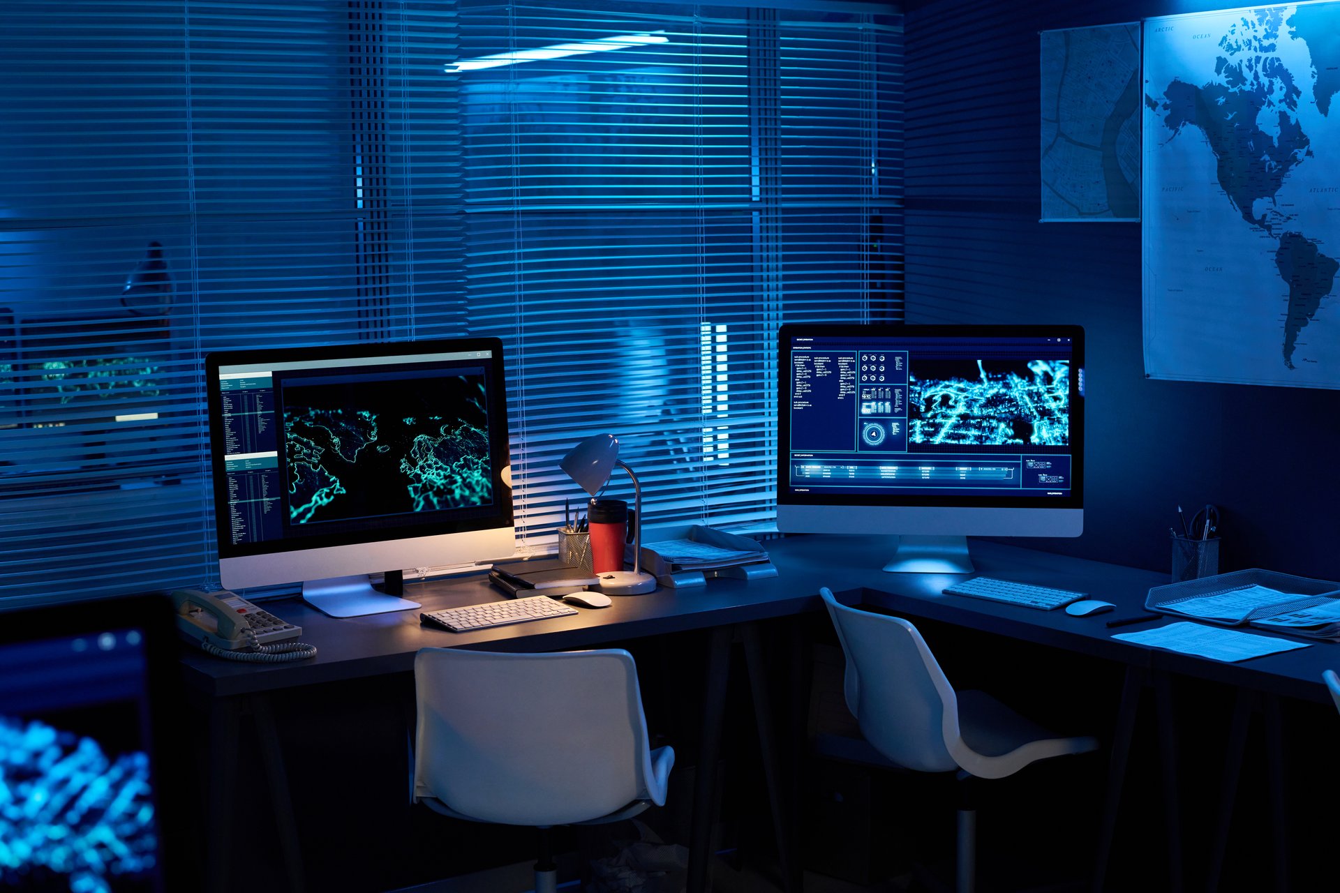 Two desktop computers with graphic data standing on desks in dark office lit with blue light in military command center