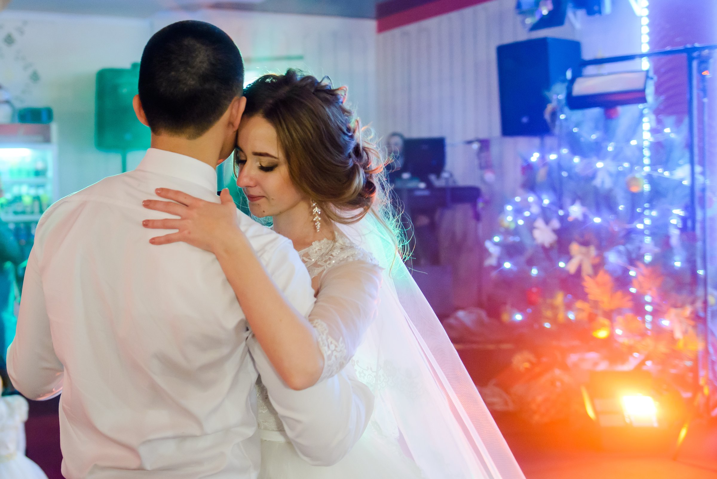 Bride and groom dancing tenderly at wedding party. Romantic first dance with colorful lights and emotional atmosphere