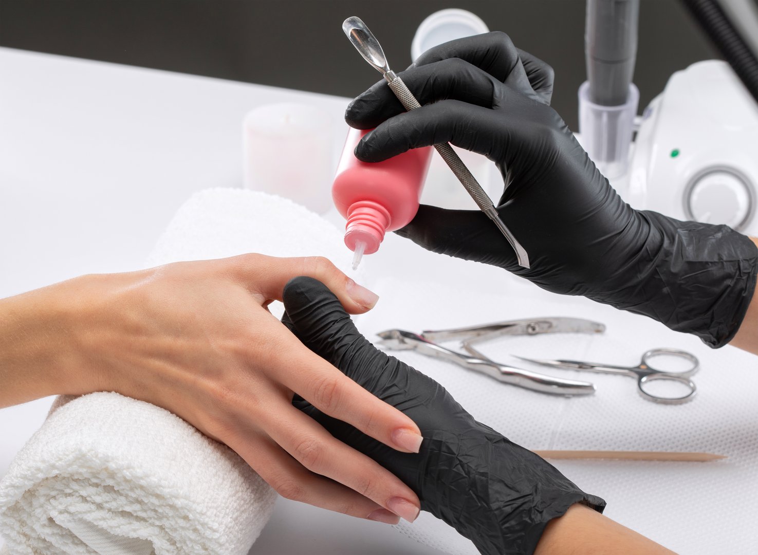Técnico de uñas aplicando esmalte con guantes de nitrilo negros resistentes a acetona en salón de belleza.