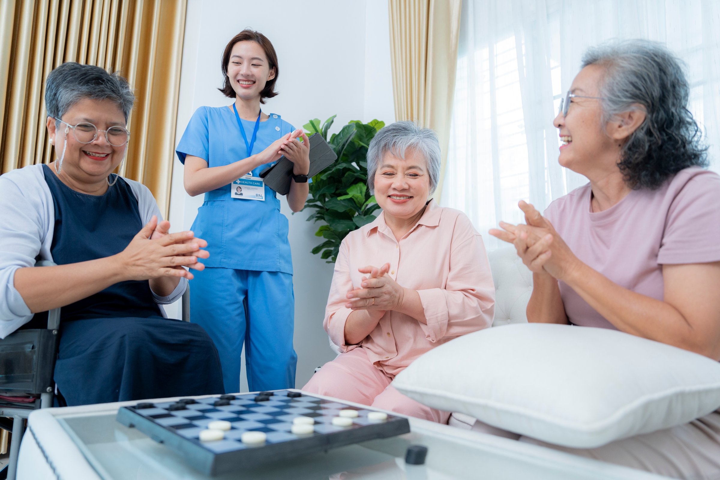 A group of elderly women enjoy a board game together, fostering social interaction and mental stimulation. A healthcare worker stands nearby, ensuring a supportive and healthy environment for senior.