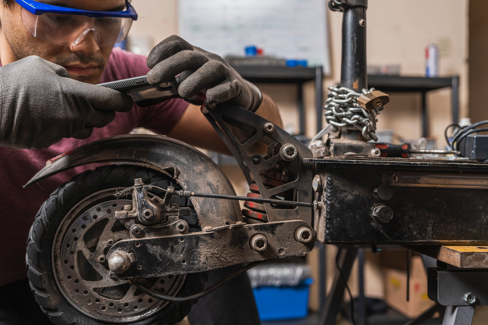 A mechanic with safety goggles taking a photo of a malfunction on an electric scooter in the workshop.