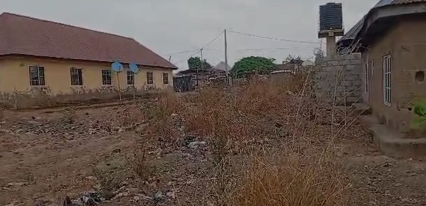 A dusty yard with dry grass between two buildings, one with a satellite dish, and a water tank on a rooftop.
