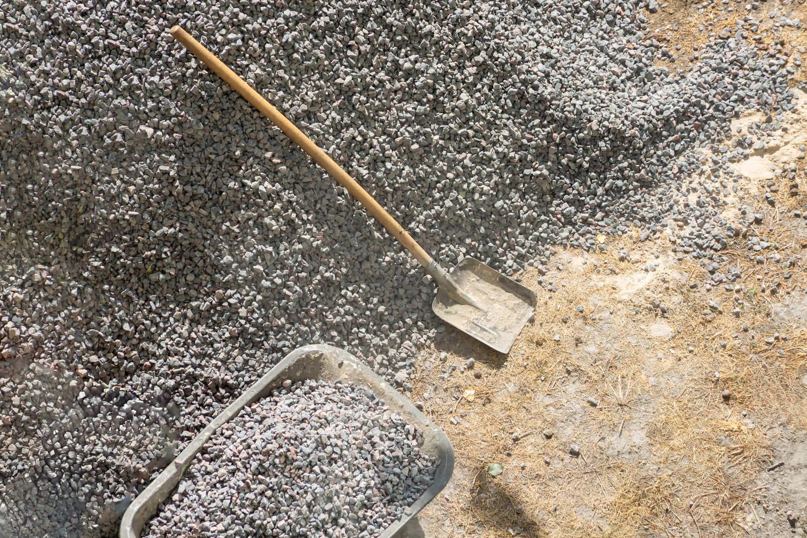 Shovel lies on large pile of gravel next to wheelbarrow filled with gravel