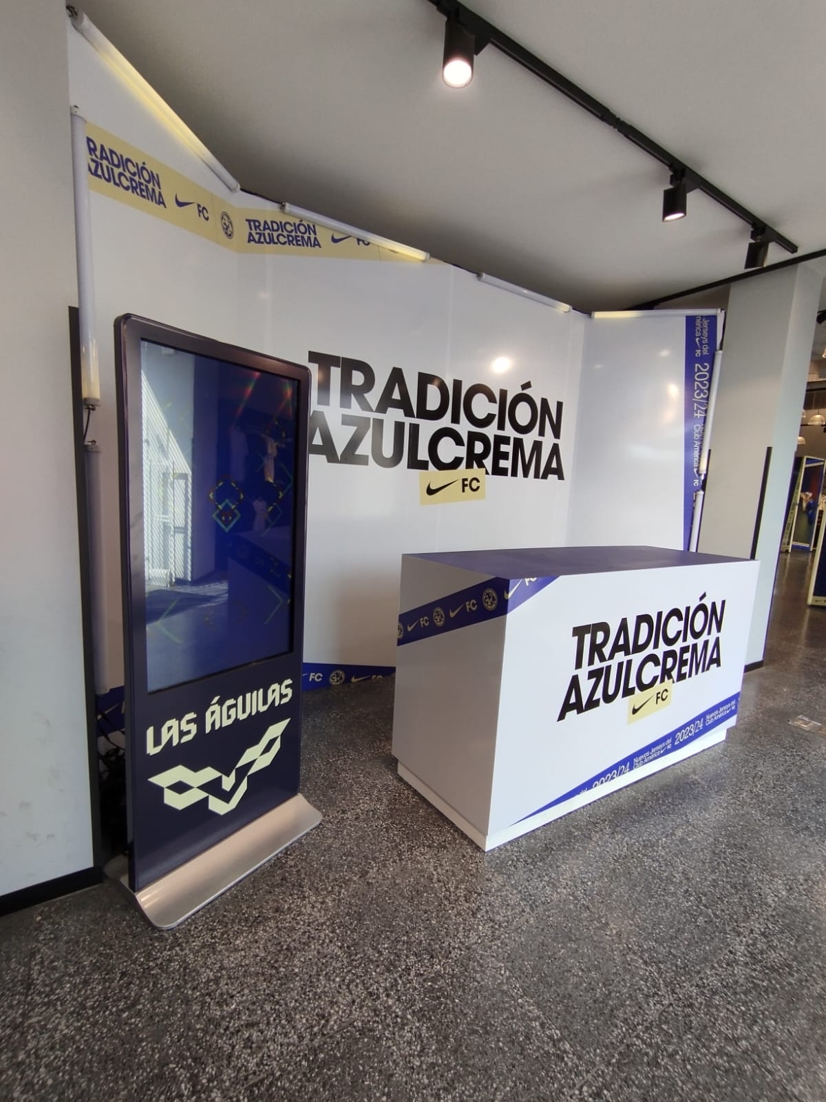 Nike-sponsored display with 'Tradición Azulcrema' and 'Las Águilas' logos, featuring a kiosk and decorated backdrop.
