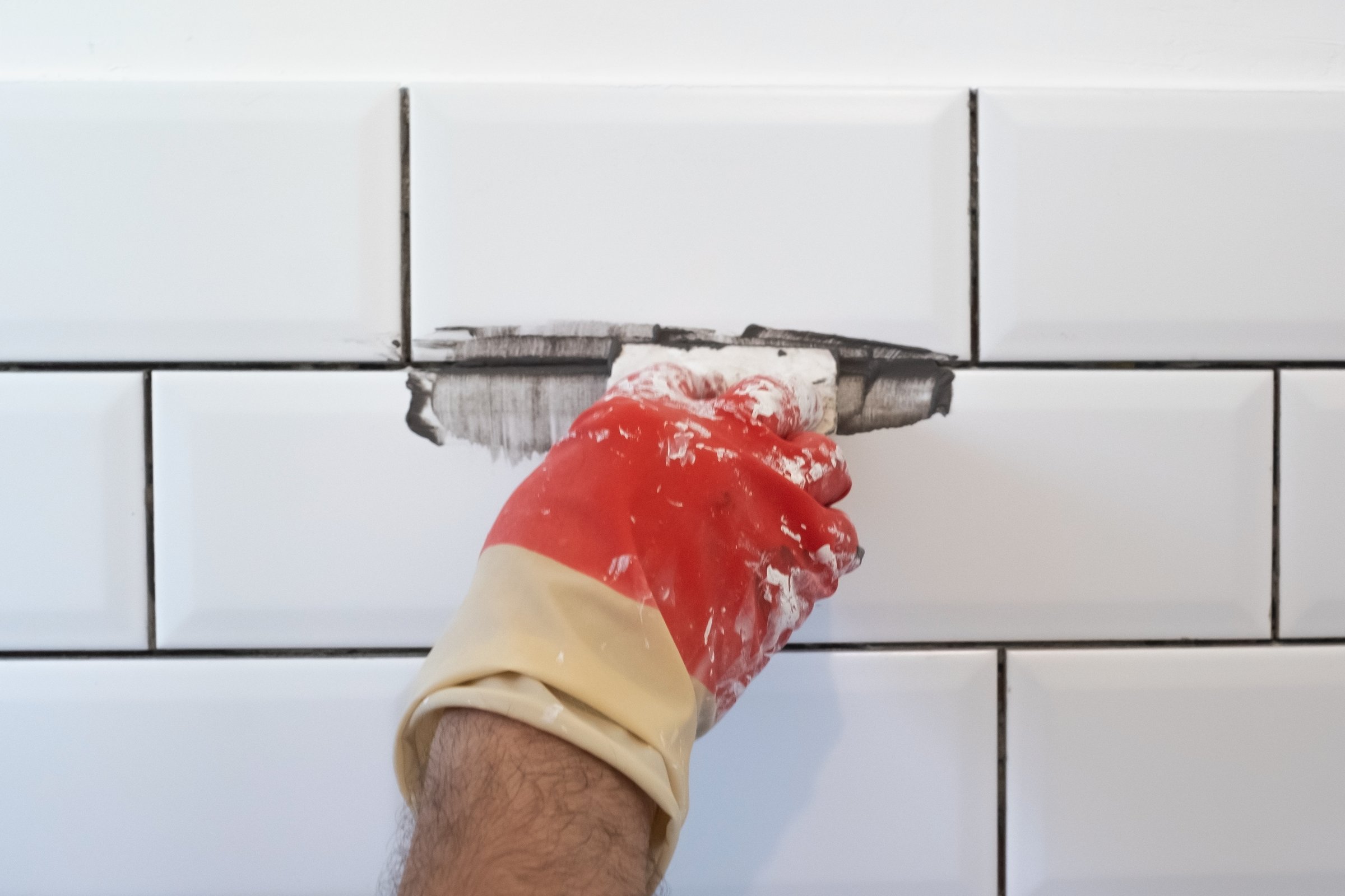 Worker applies grey grout at white tiles with rubber trowel. Kitchen renovation.