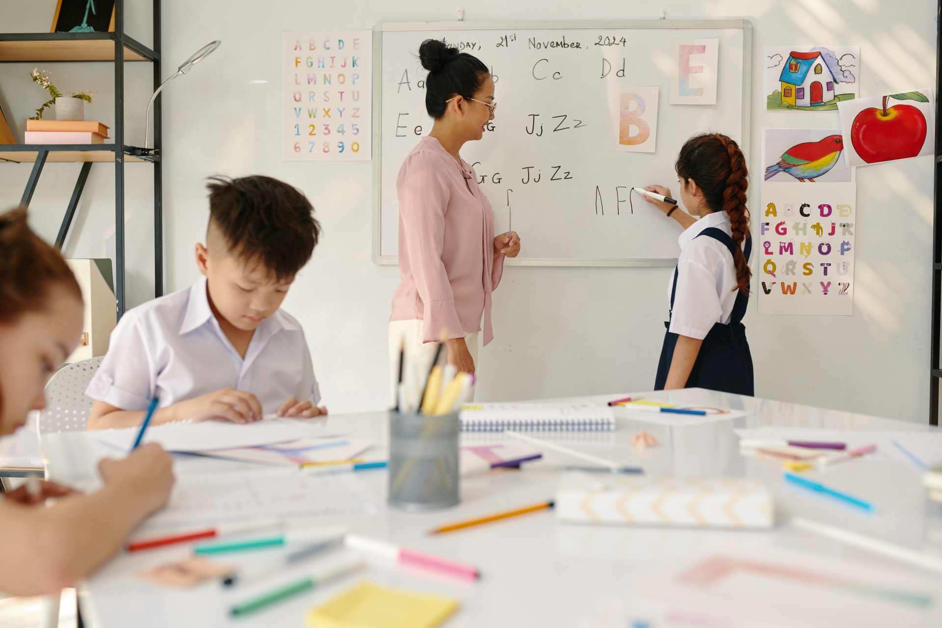 Schoolgirl writing on whiteboard letter that teacher asks her
