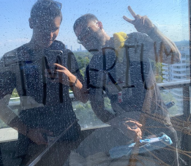 Two people on a balcony, reflecting on a glass panel with "IMPERRI" written in condensation.