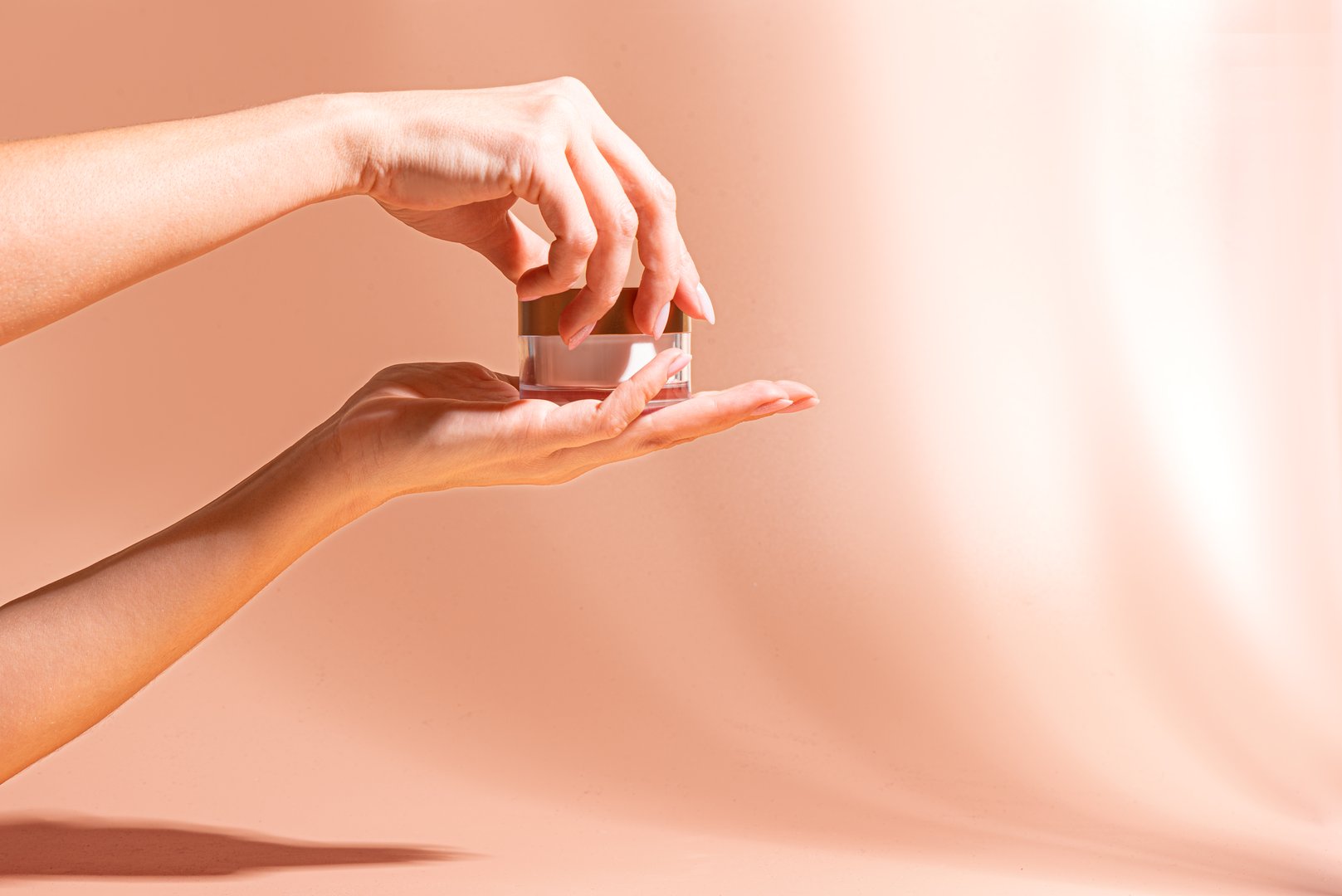 Female hands hold and open face cream jar, beige background with shadows, copy space. Woman applying moisturizer cosmetic product, daily beauty routine.
