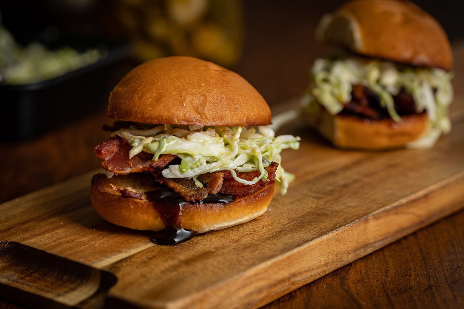 Pork belly sliders with cabbage slaw and sauce dripping from the bottom bun placed on wooden cutting board
