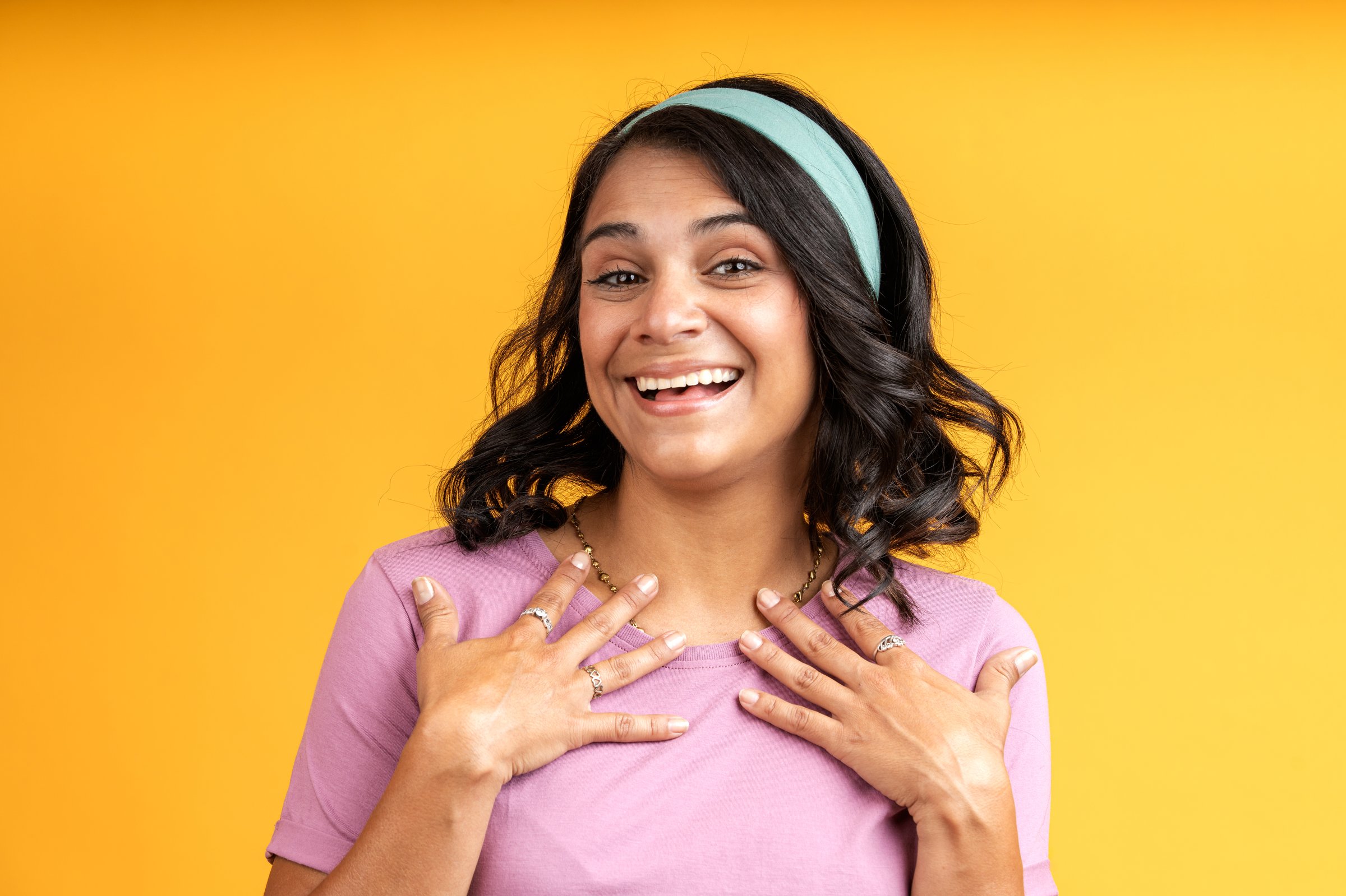 Excited young woman expressing gratitude and happiness with hand gestures on a vibrant yellow background