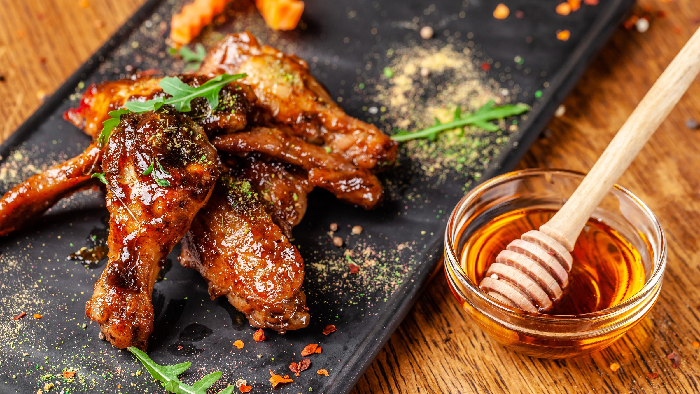 The concept of Indian cuisine. Baked chicken wings and legs in honey mustard sauce. Serving dishes in the restaurant on a black plate. Indian spices on a wooden table. background image.
