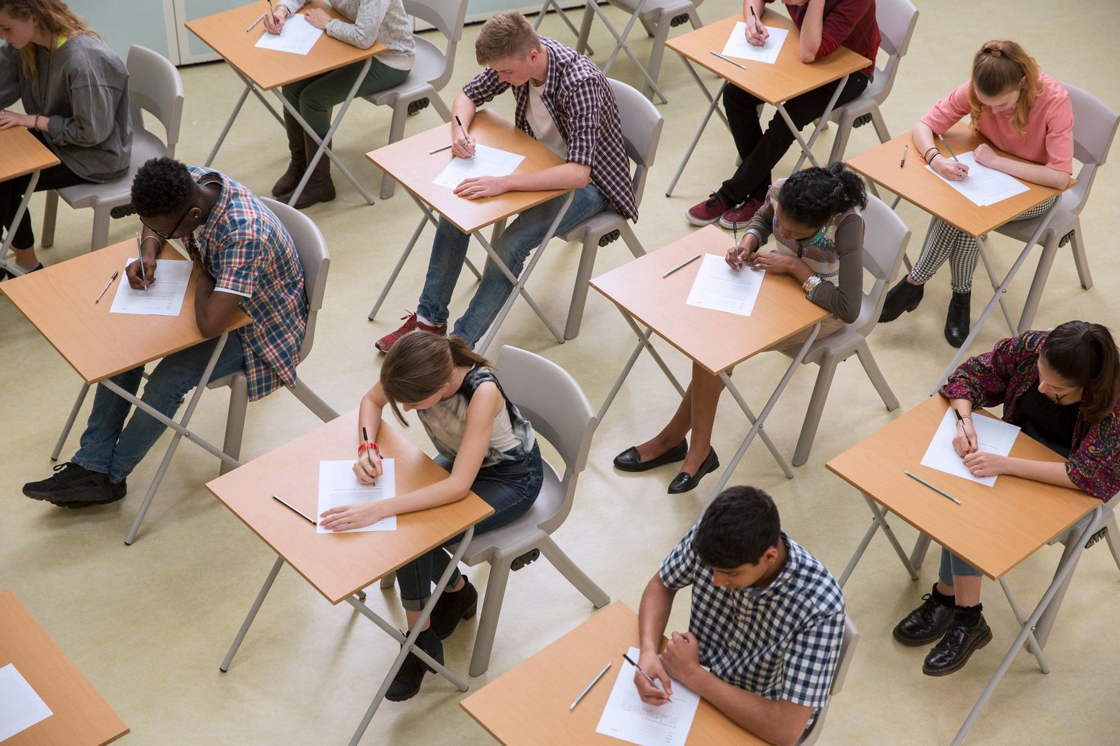 Students seated in a classroom taking an exam at individual desks, focused on writing on their papers.
