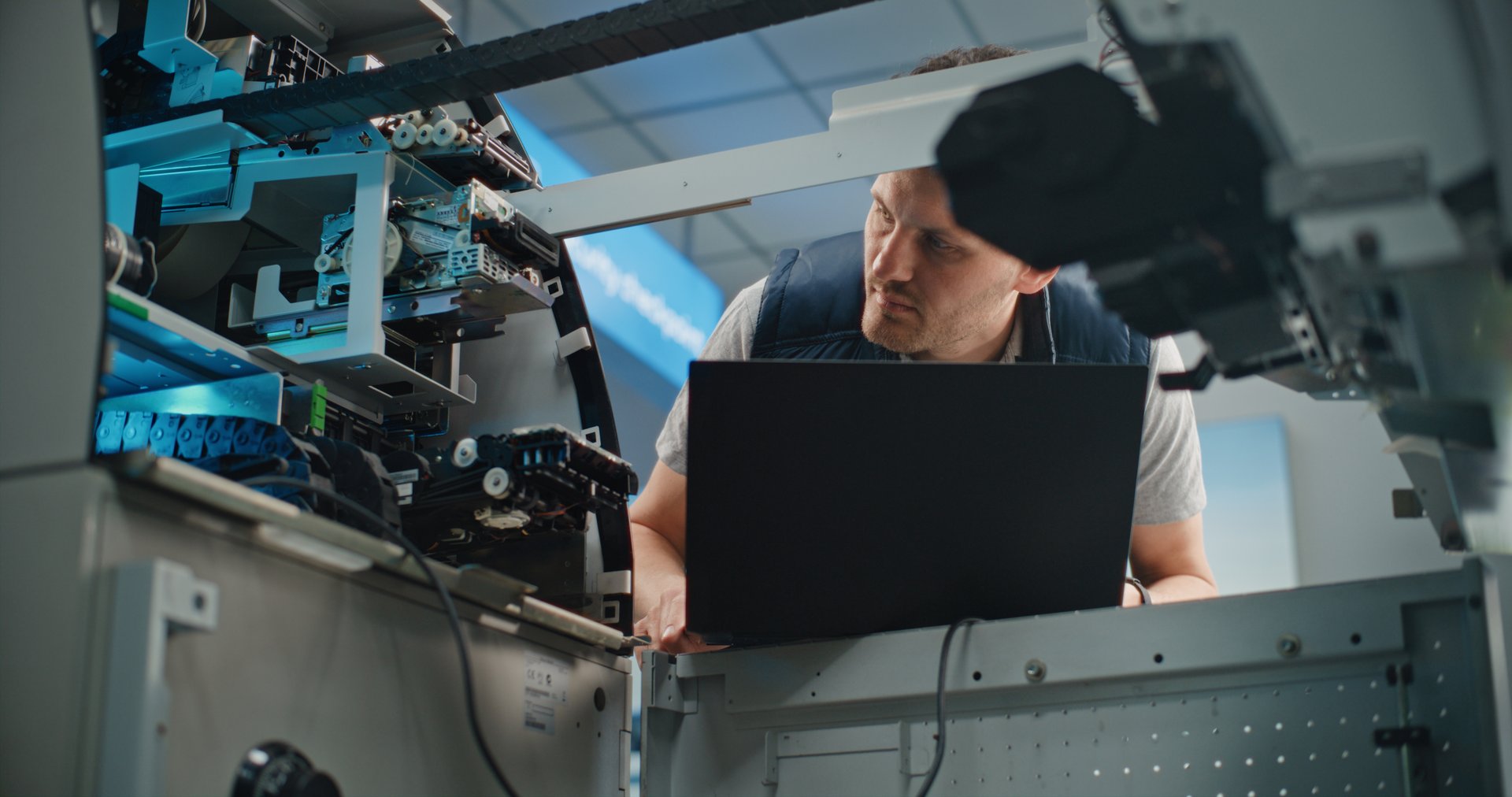 ATM Technician in Uniform Servicing Cash Dispenser Machine in Modern Airport Terminal. Male Worker Conducting Diagnostics of ATM Machine Using Laptop. Banking, Cash Withdrawal Systems and ATM Repair.