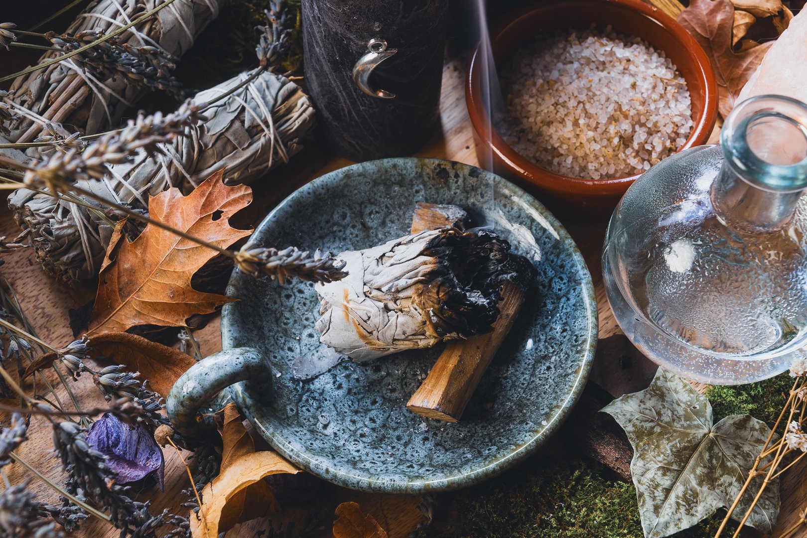 Close-up of a mystical Wiccan altar with smudge stick, herbs, salt, and ritual tools surrounded by dried leaves and crystals