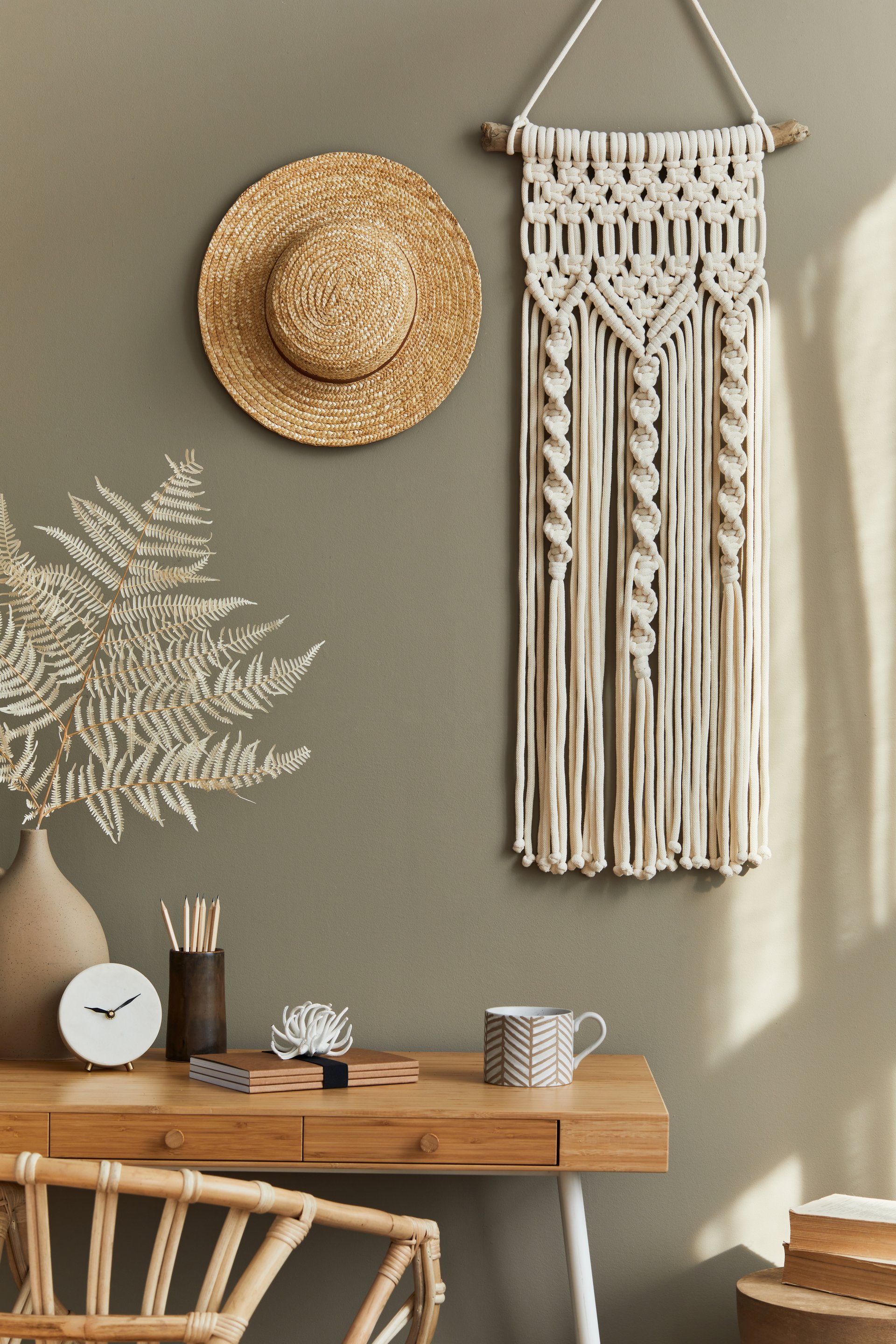 Stylish bohemian interior of home office space with wooden desk, office supplies, decoration and elegant personal accessories in home decor.