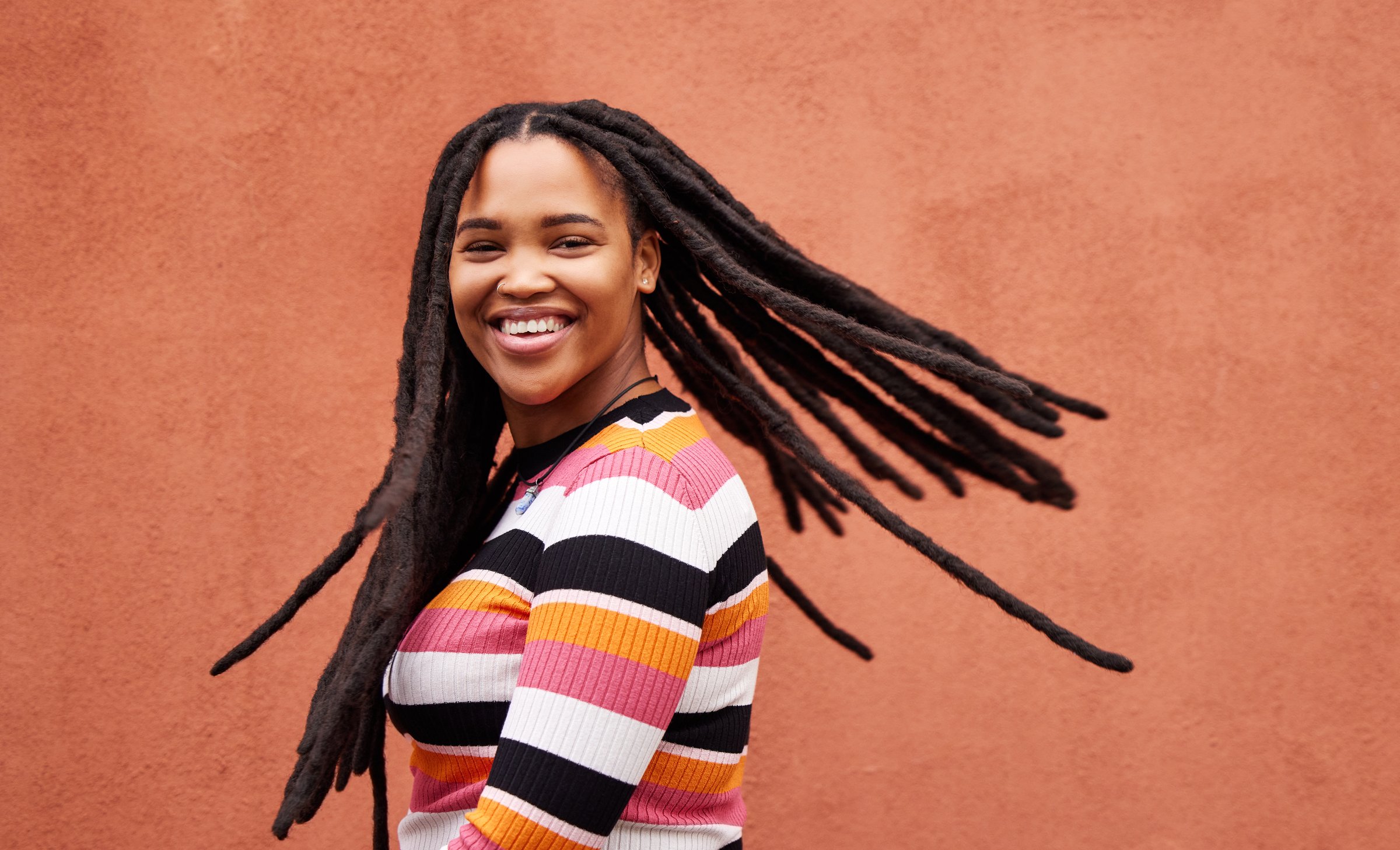 Playful, fun and portrait of a black woman with a smile isolated on a studio background. Happy, laughing and a funny young African girl with dreadlocks, happiness and expression on a backdrop