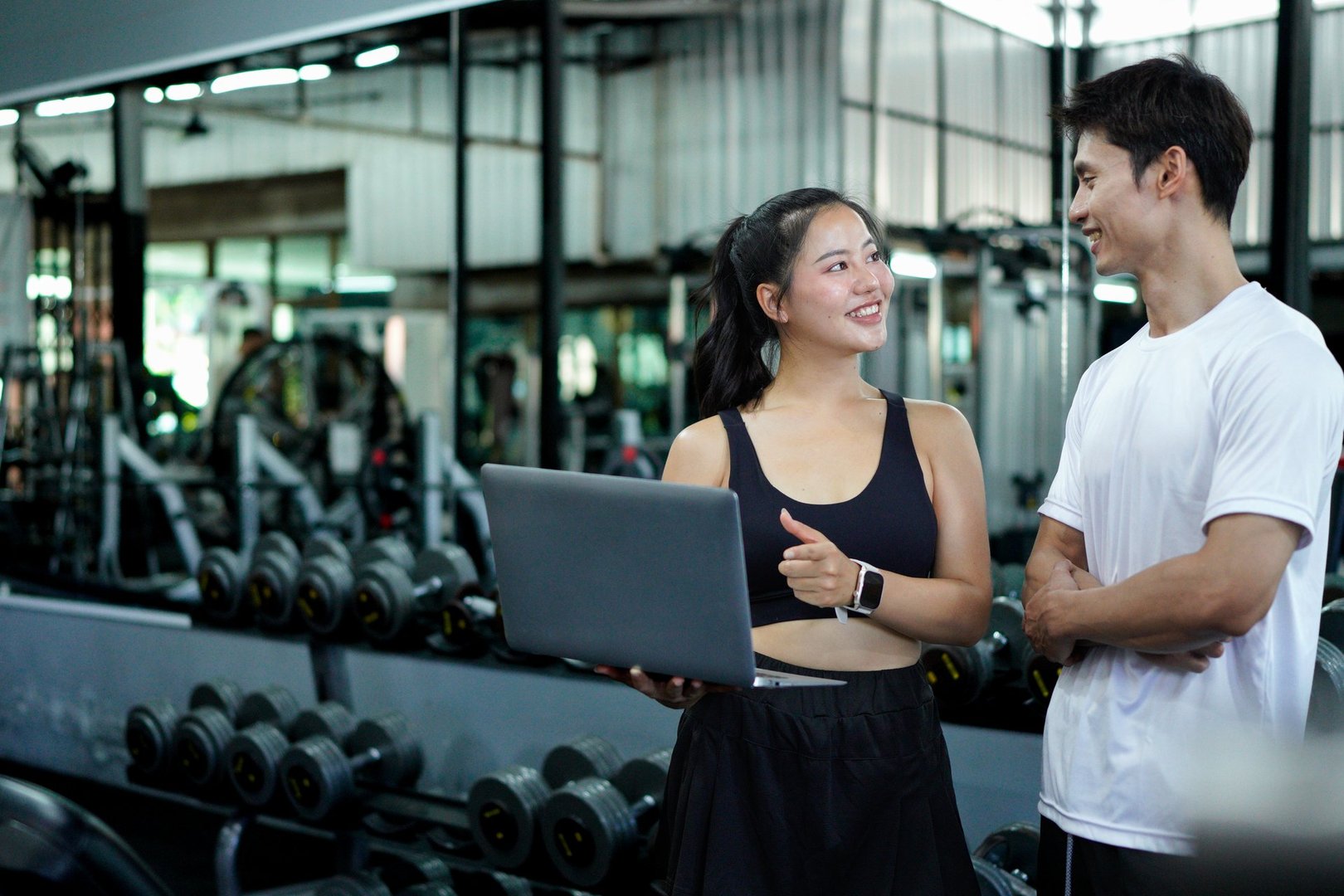 Asian man and woman exercise training in fitness gym. Young female trainer using laptop for schedule exercise training to fitness male. Workout training in fitness gym..