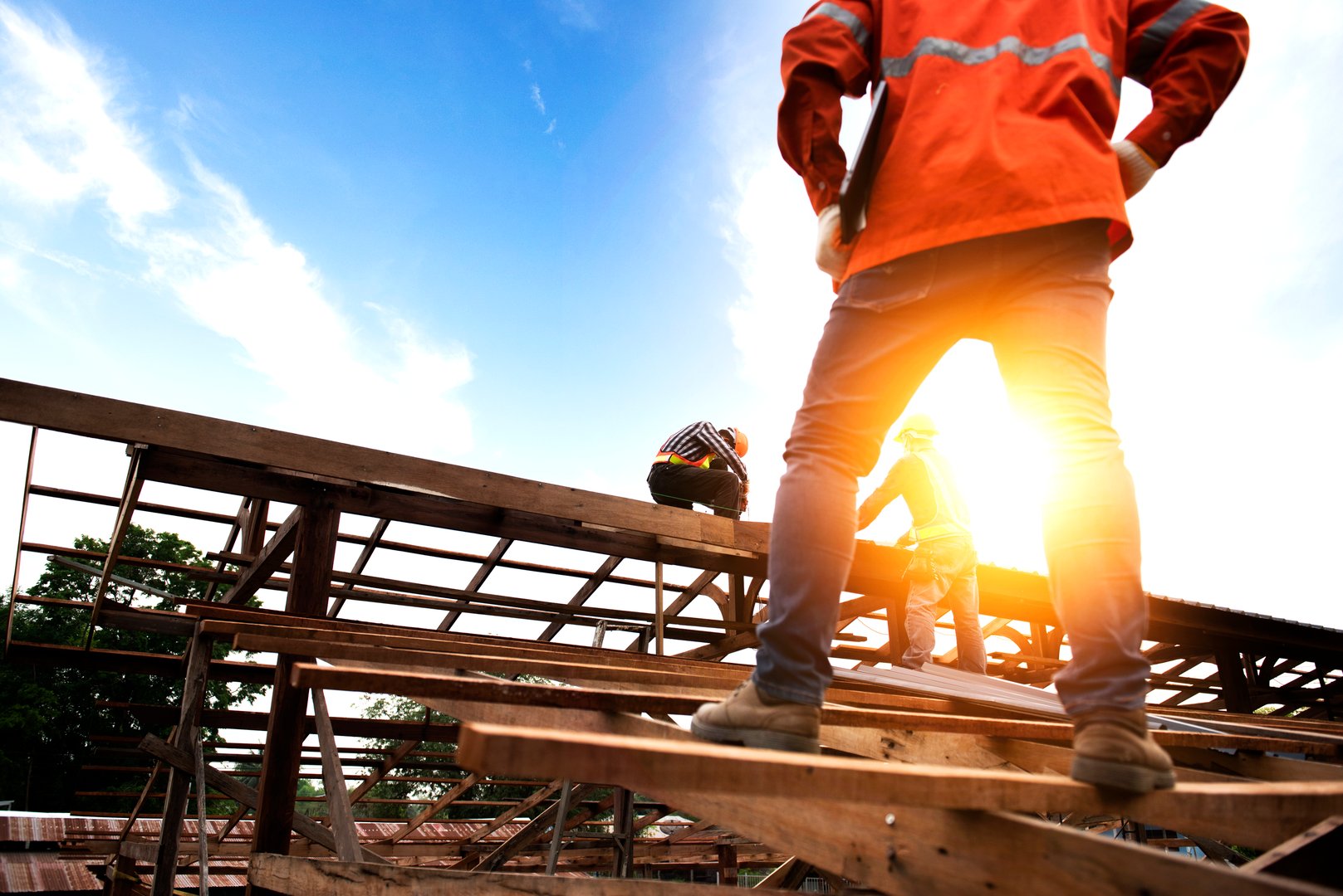 A photograph of an engineer in a hard hat holding a laptop and looking at a team of wood roofers on the construction site.