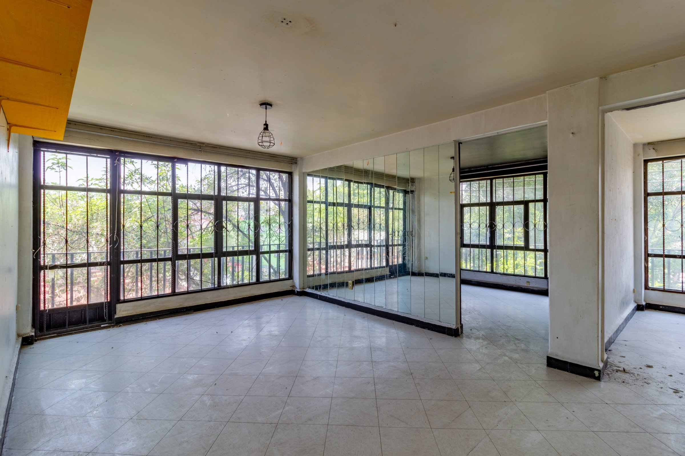 Empty room with tiled floor, large windows, mirrored wall, minimal fixtures, and natural light from outdoors.