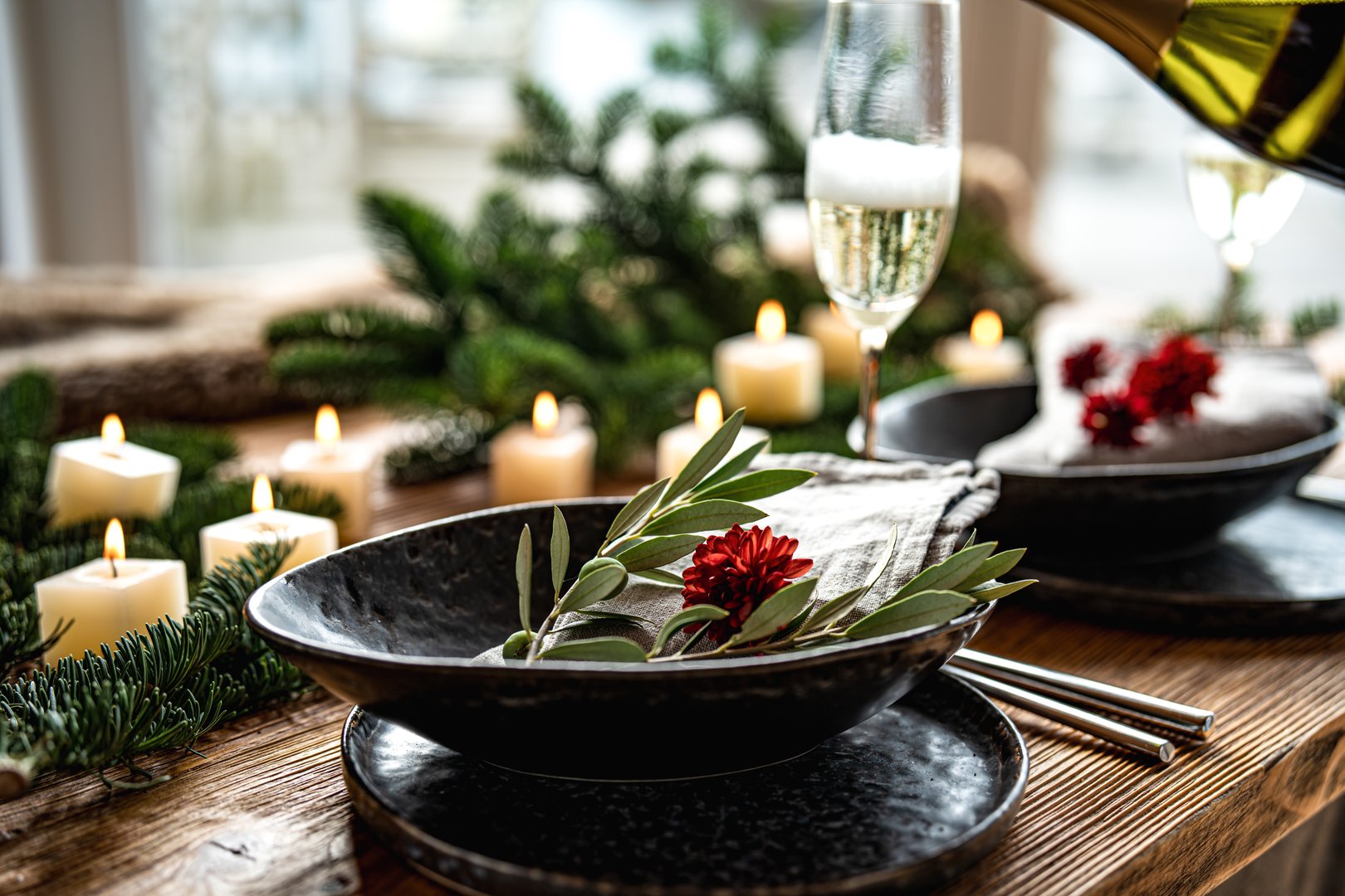Table decoration for festive occasions and invitations. Pouring champagne into the glass and candlelight on a rustic wooden table with green branches. Background for christmas gastronomy and lifestyle.