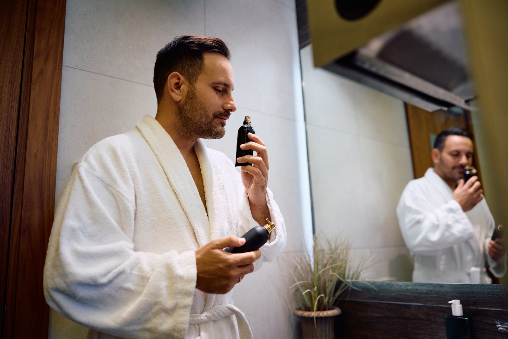 Smiling man in bathrobe choosing perfume after a bath.