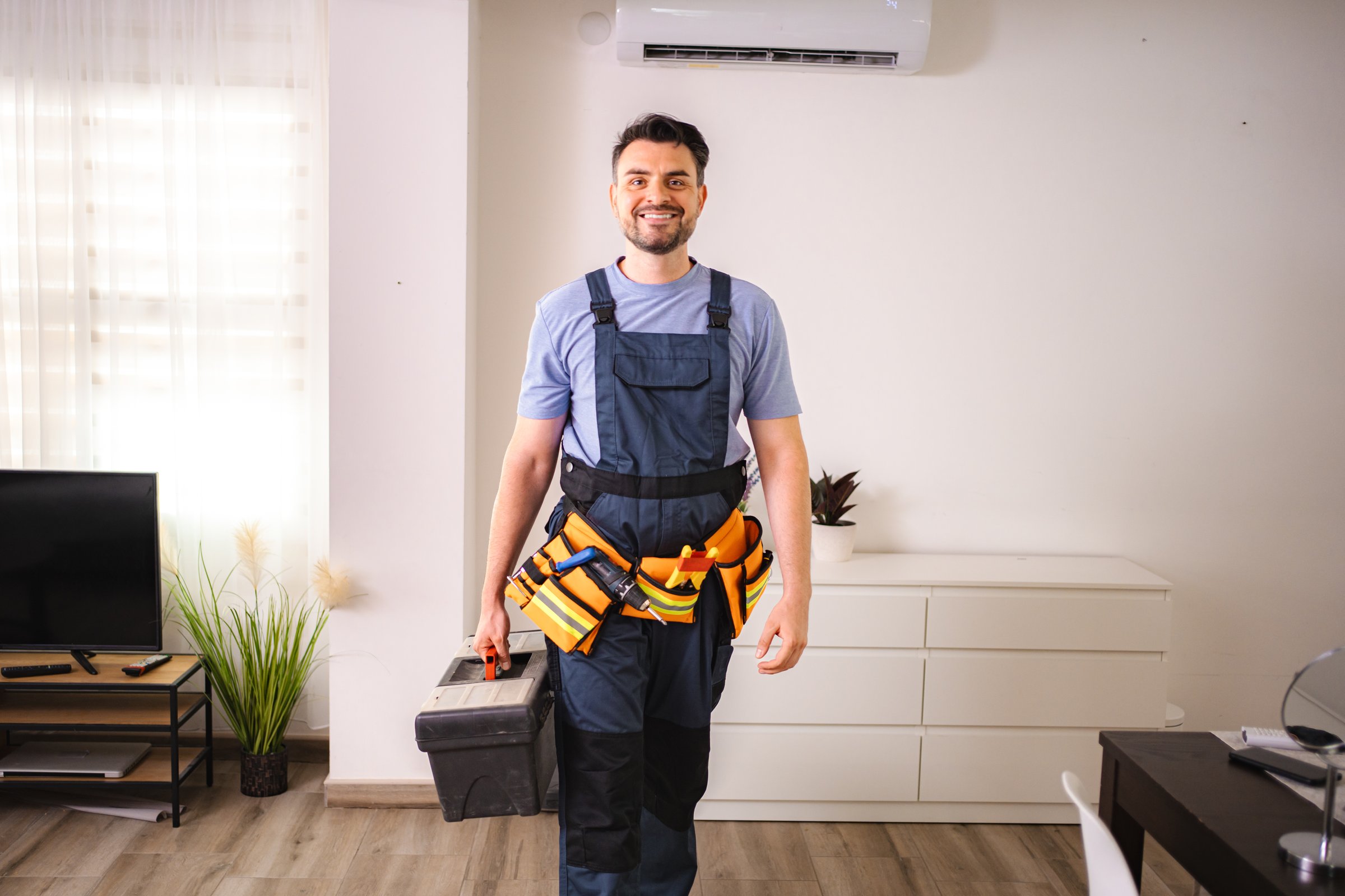 Smiling technician walking and carrying toolbox and wearing tool belt in a home