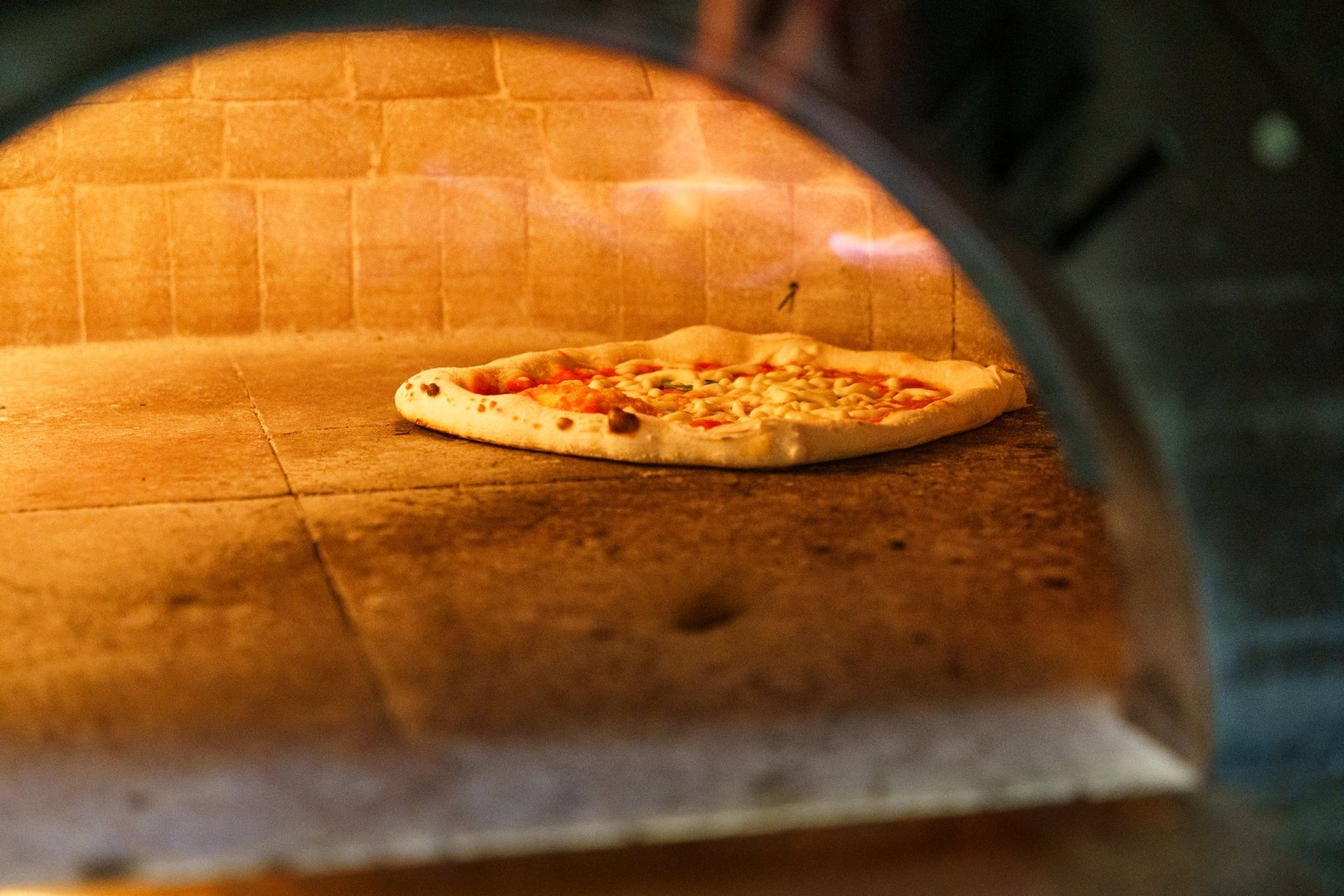 A freshly prepared Neapolitan pizza is baking inside a traditional oven, with its crust beginning to rise and char, emphasizing the authentic cooking process of Italian-style pizza.