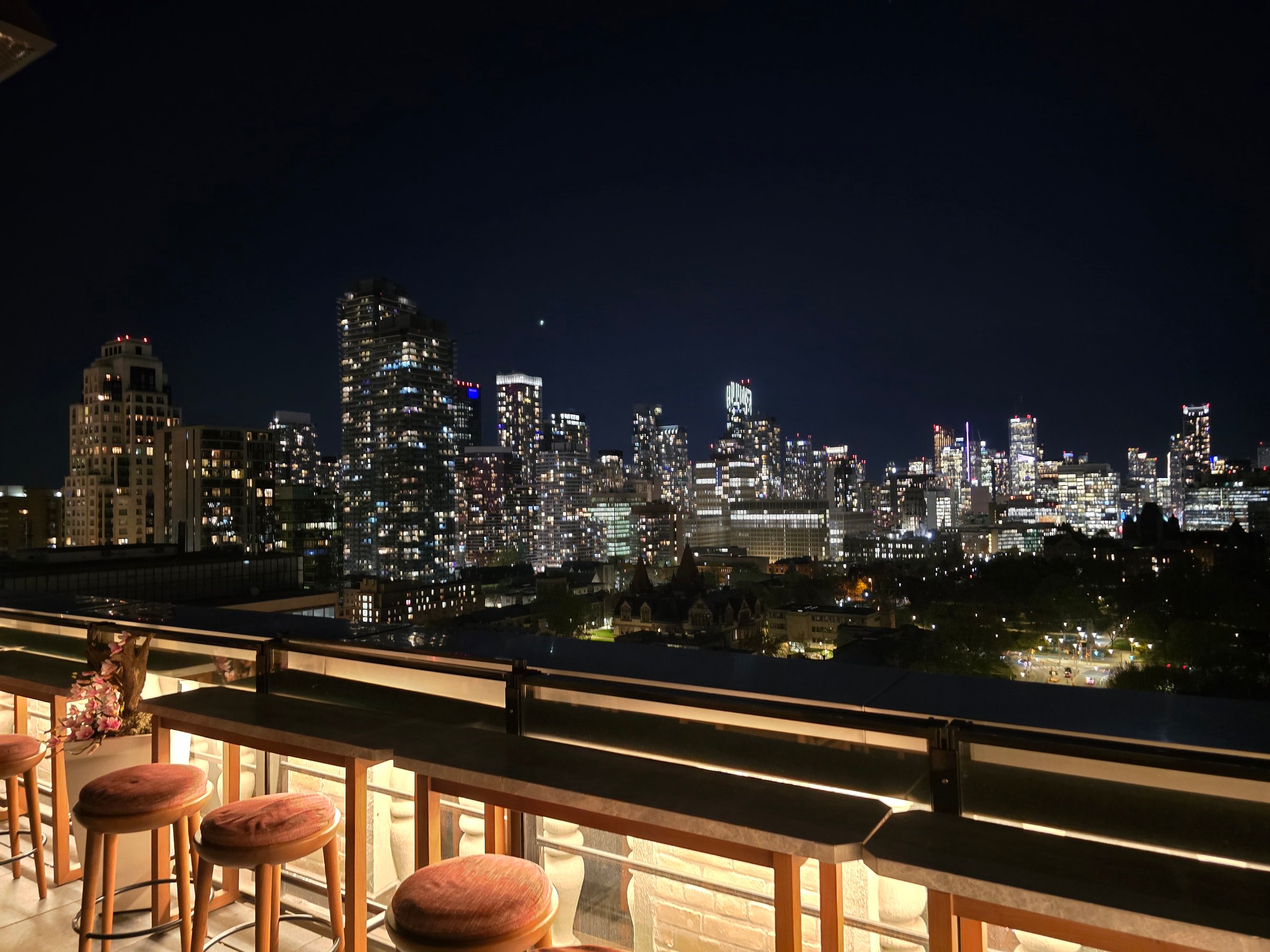 Beautiful city skyline at night seen from a rooftop bar with cozy seating and glowing lights. Urban nightlife, high-rise buildings, and downtown view create a stunning modern atmosphere.