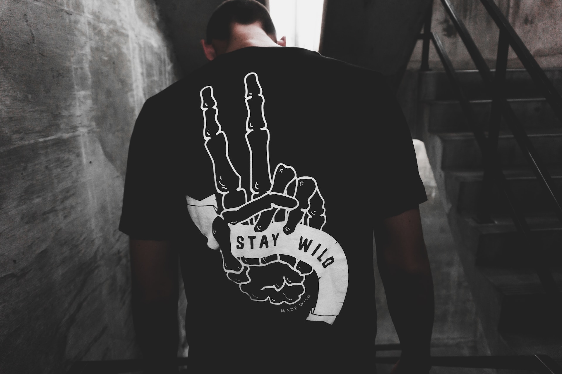 Person wearing a black t-shirt with a skeleton hand design showing a peace sign and the words Stay Wild on the back.