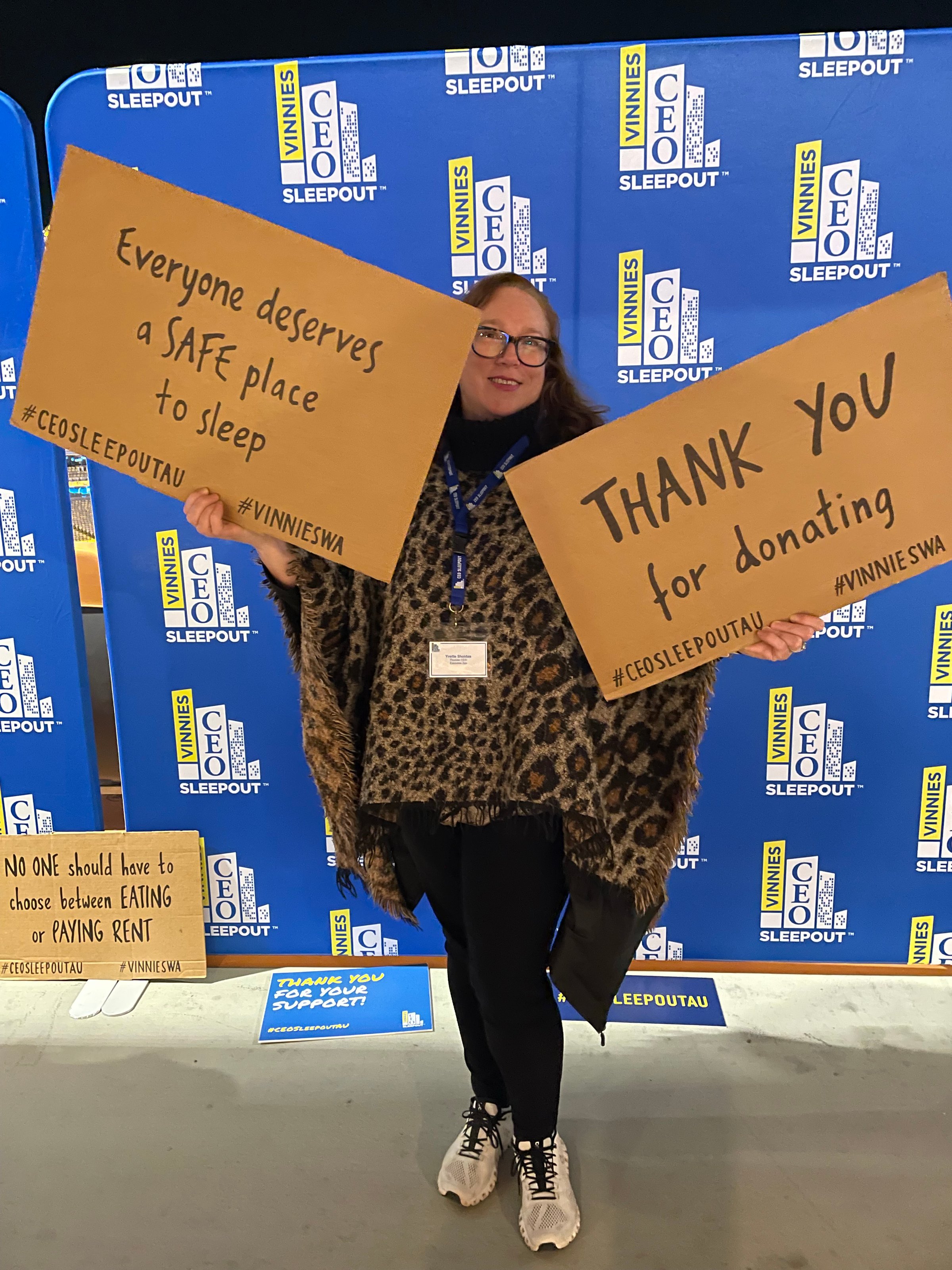 Person holds signs supporting safe sleeping and donations at a charity event with a blue banner background.