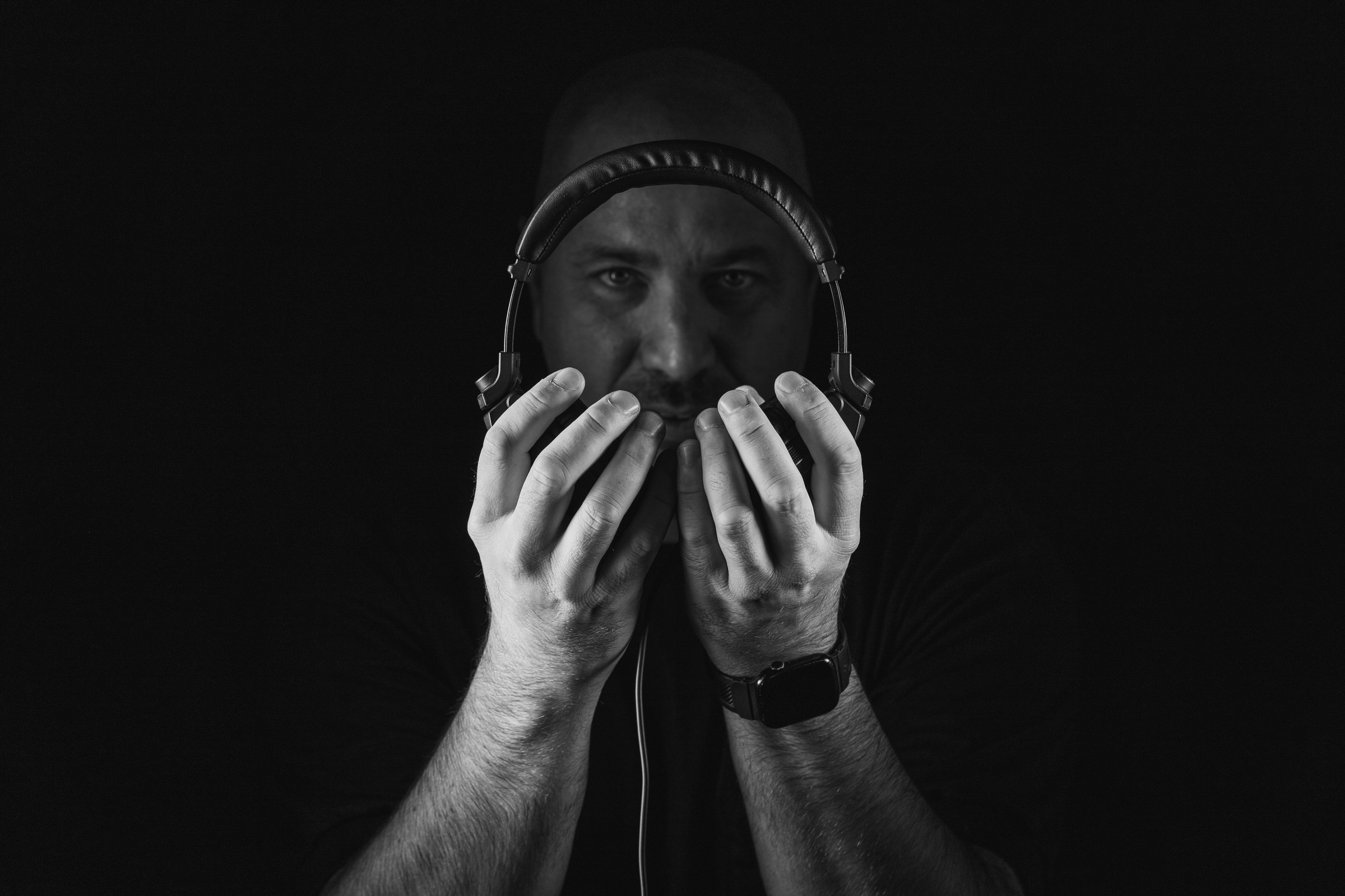Black and white photo of a person holding headphones in front of their face against a dark background.
