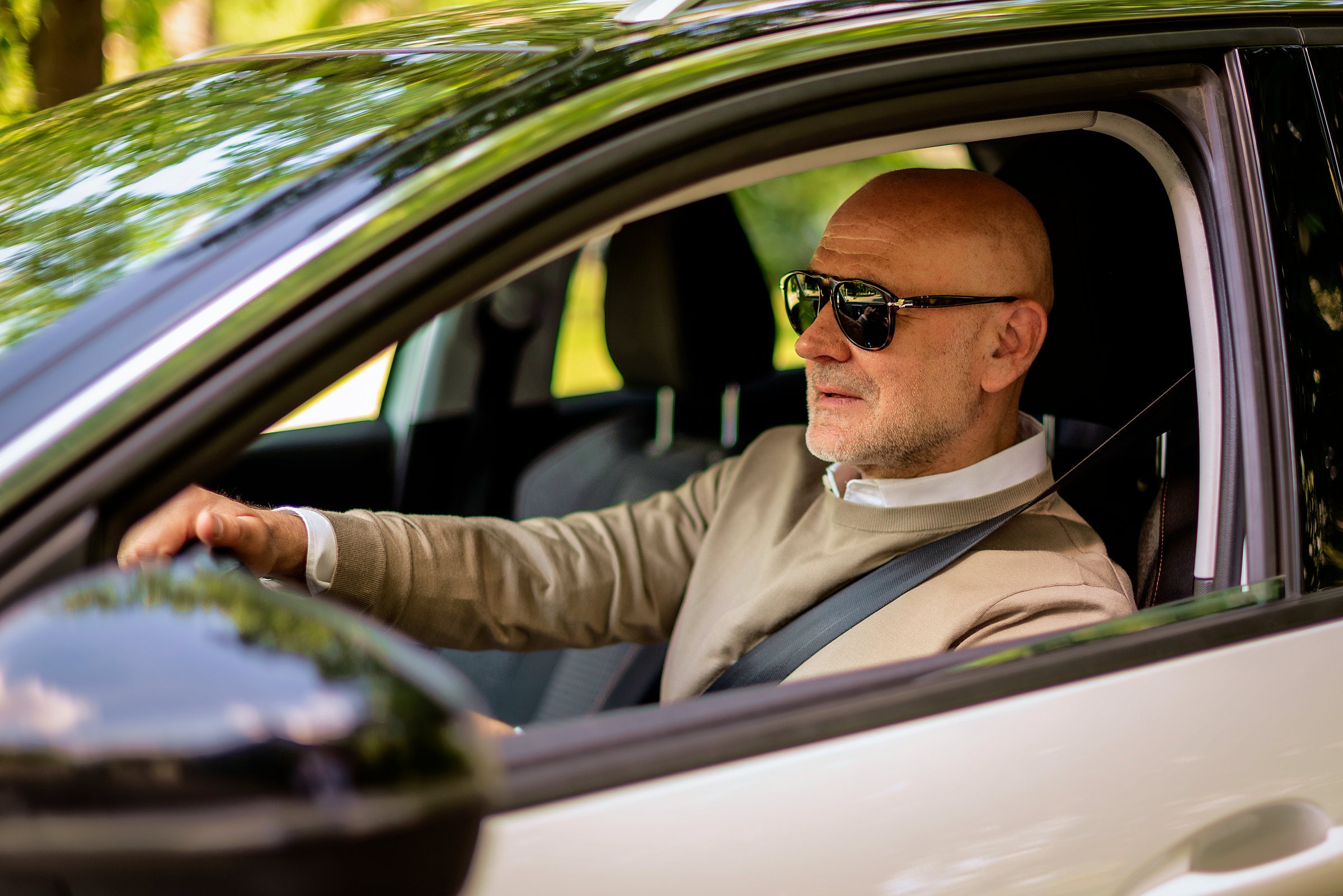 A mature man with sunglasses driving in a modern car in the city.