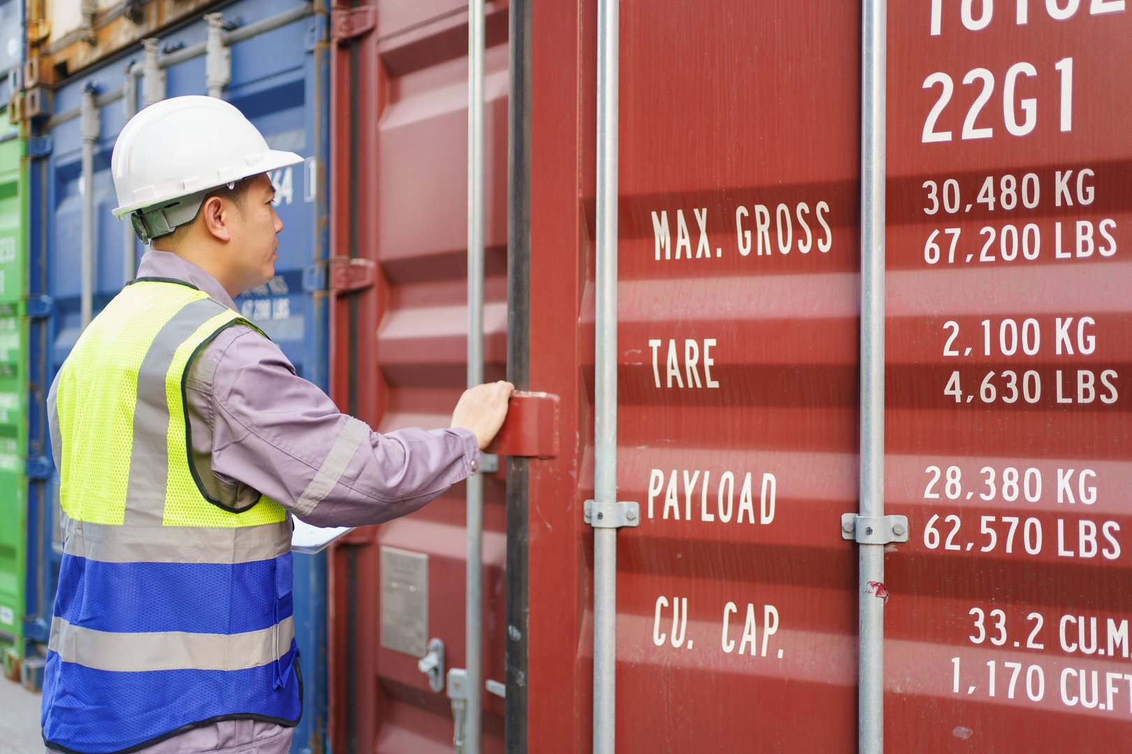 Asian male shipyard engineer is inspecting import or export cargo containers at the container yard. A customs clearance officer inspects against the import - export cargo.
