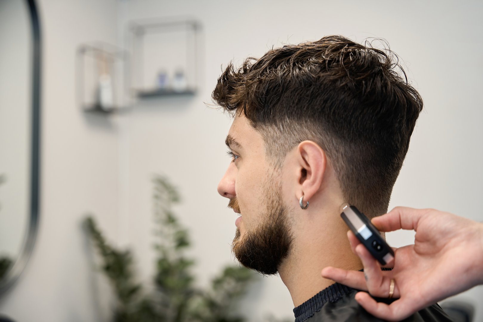 Close up photo of barber, standing near smiling man, holding shaver and cutting hair