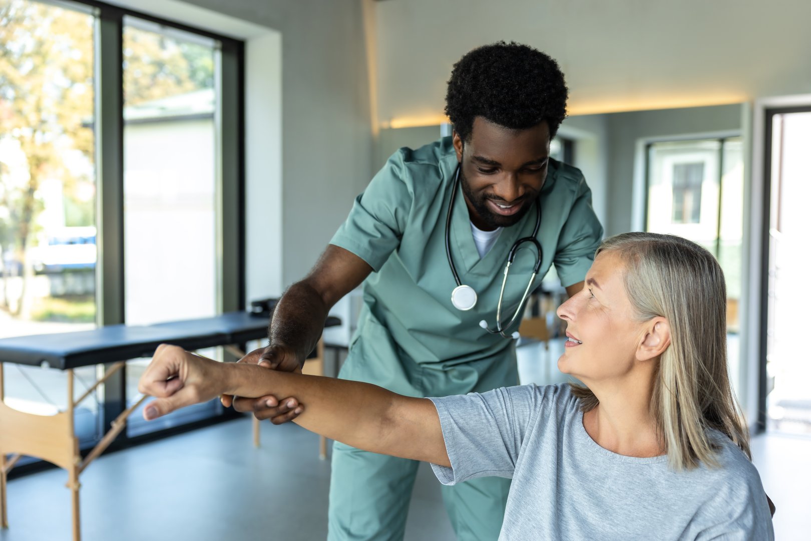 African American man chiropractor assisting adult woman patient with pain relief and recovery through physiotherapy and rehabilitation