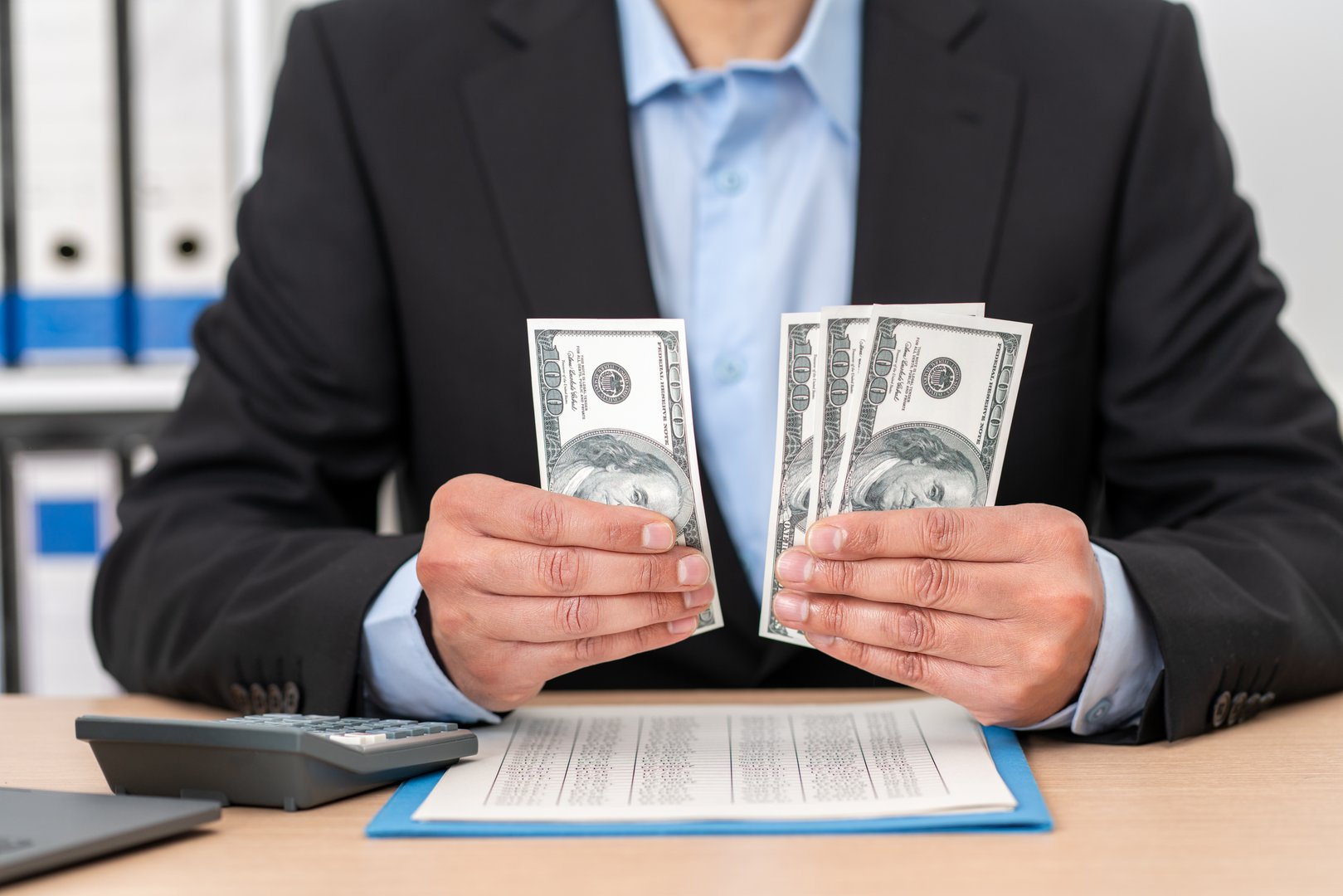 Business man, calculator and money in business finance for budget, costs or expenses at the office desk. Hands of male accountant counting and calculating cash on table for company profit.