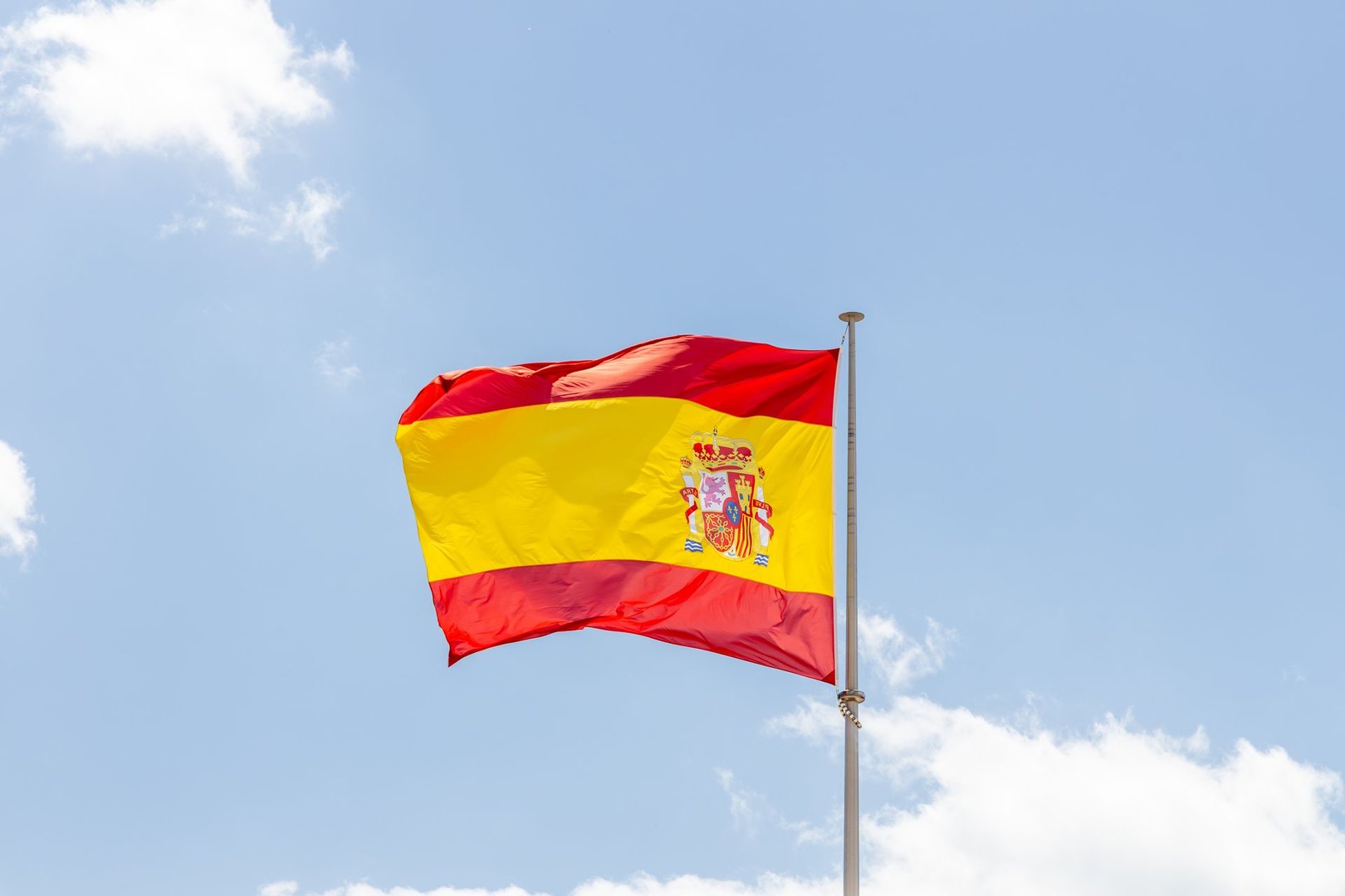 Spanish flag is waving proudly against a bright blue sky, displaying vivid colors and emblem, representing national pride and cultural identity