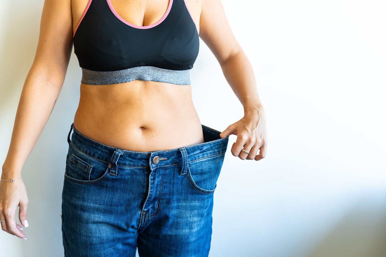 Woman proudly displaying weight loss progress by wearing oversized jeans, highlighting her transformation and newfound confidence