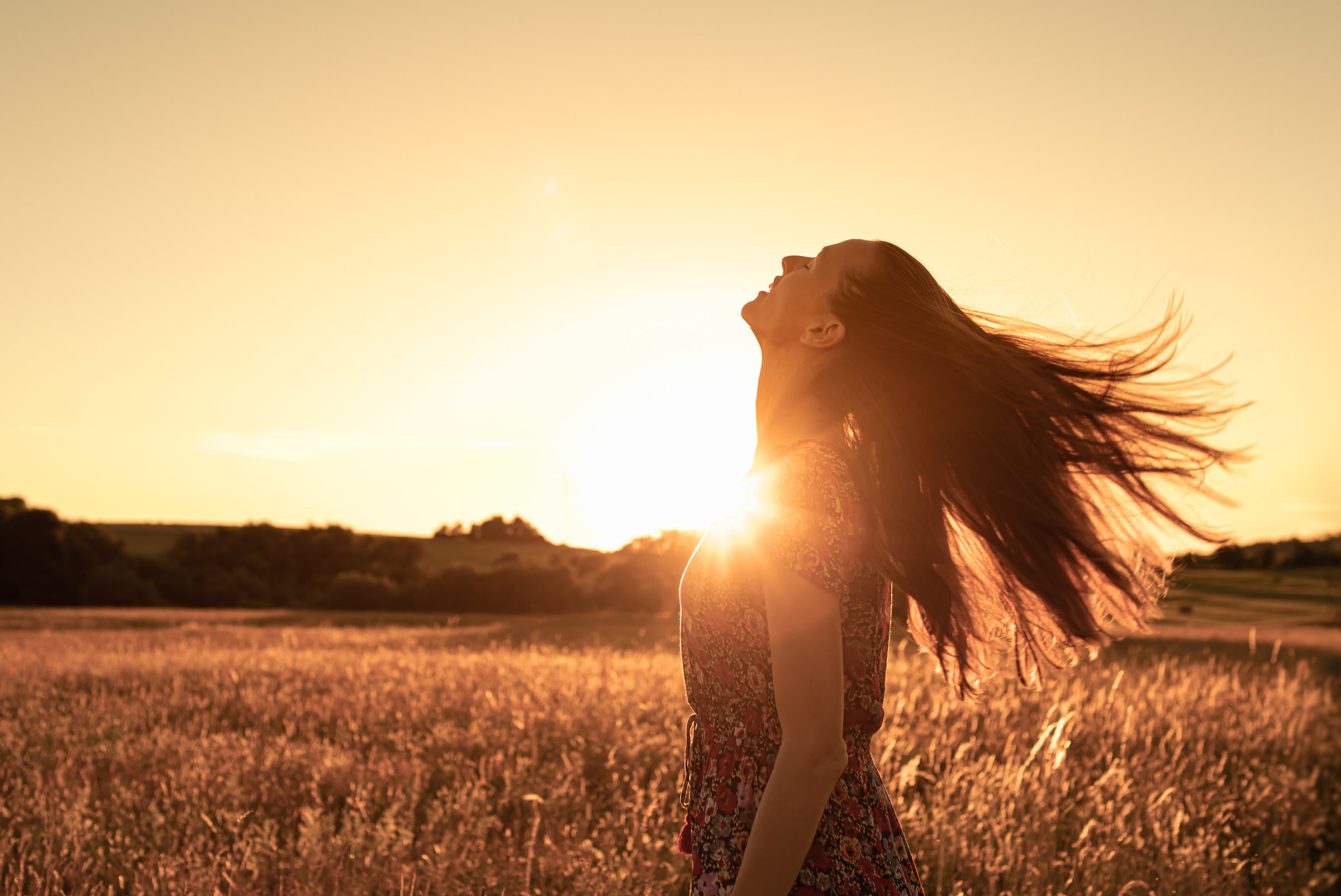 Woman in a Meadow at sunset looking up to the sky feeling joyfull