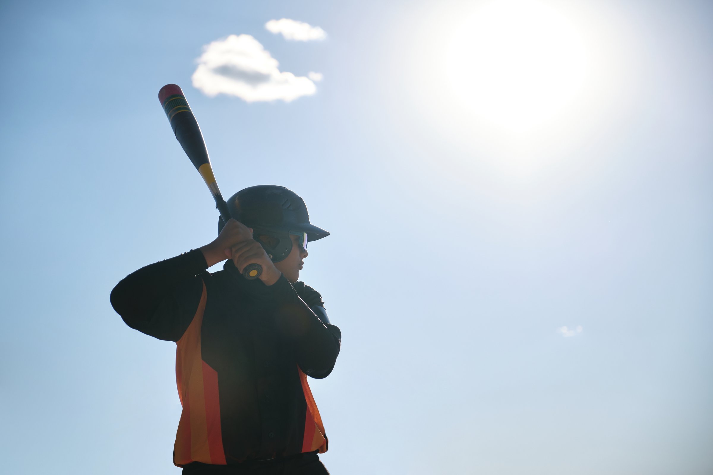 Child baseball player swinging bat in silhouette on sunny day