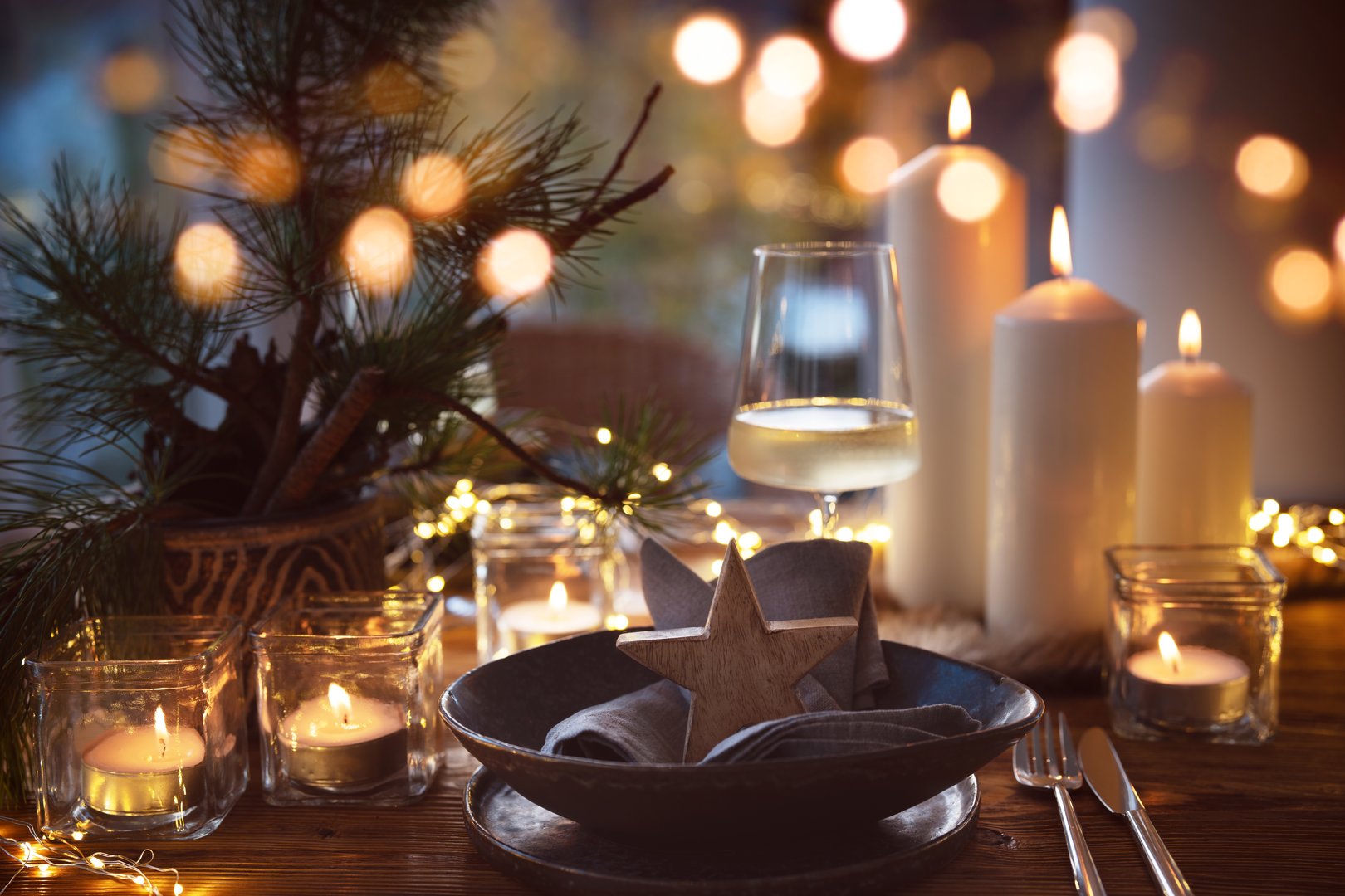 Elegant table decoration for a christmas dinner. Romantic dinner concept with burning candles in the evening at a restaurant. Close-up with golden bokeh lights. Background for seasonal an holiday gastronomy.