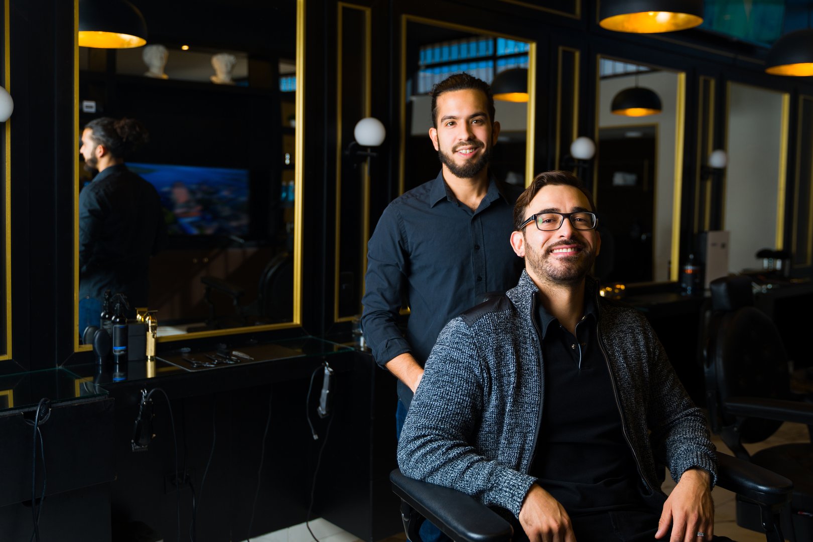 Latin hairstylist and caucasian client smiling while coming to a men's barber shop to trim his beard and cut his hair